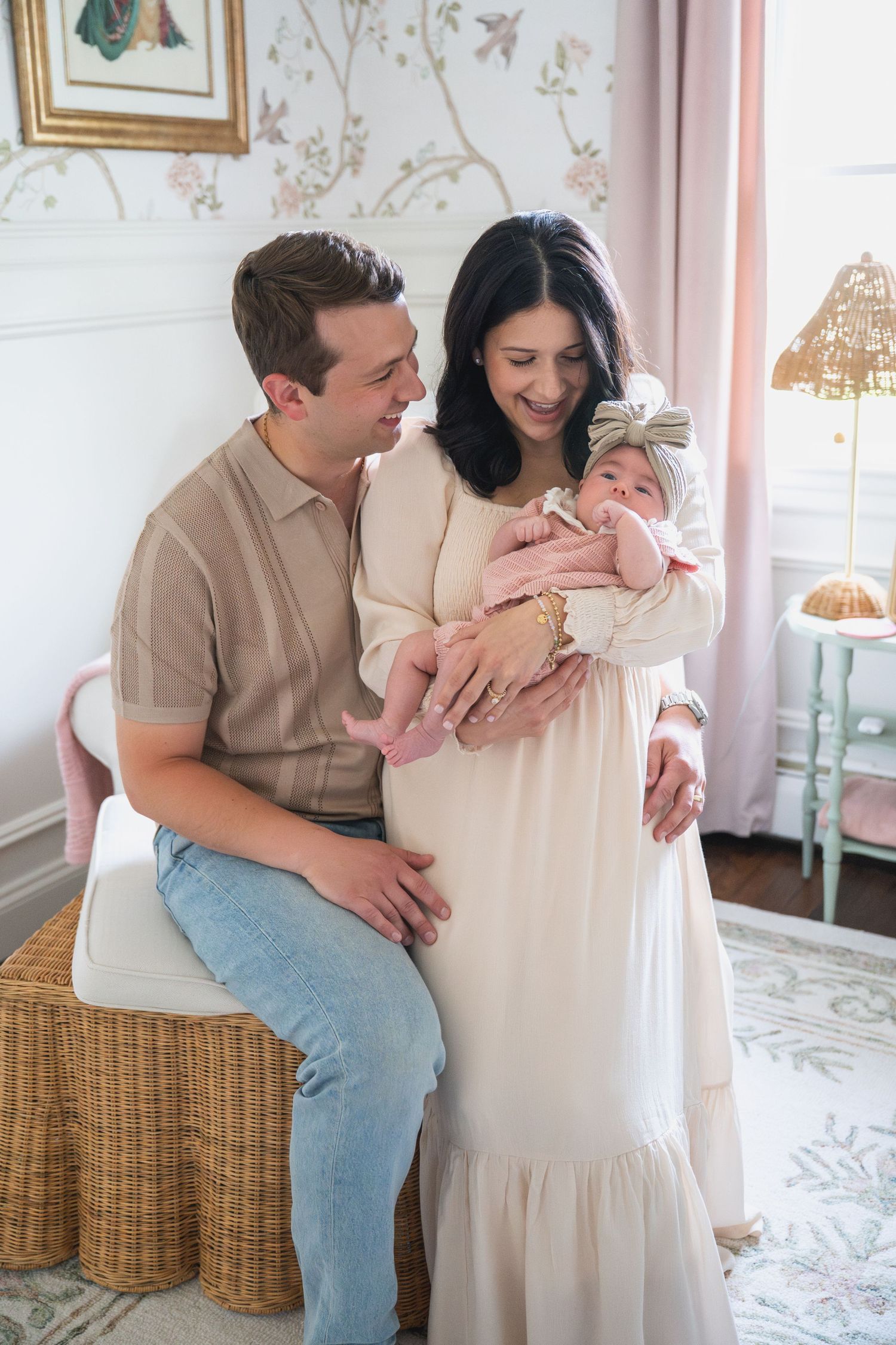 Family members share tender moments in a nursery decorated with floral wallpaper.