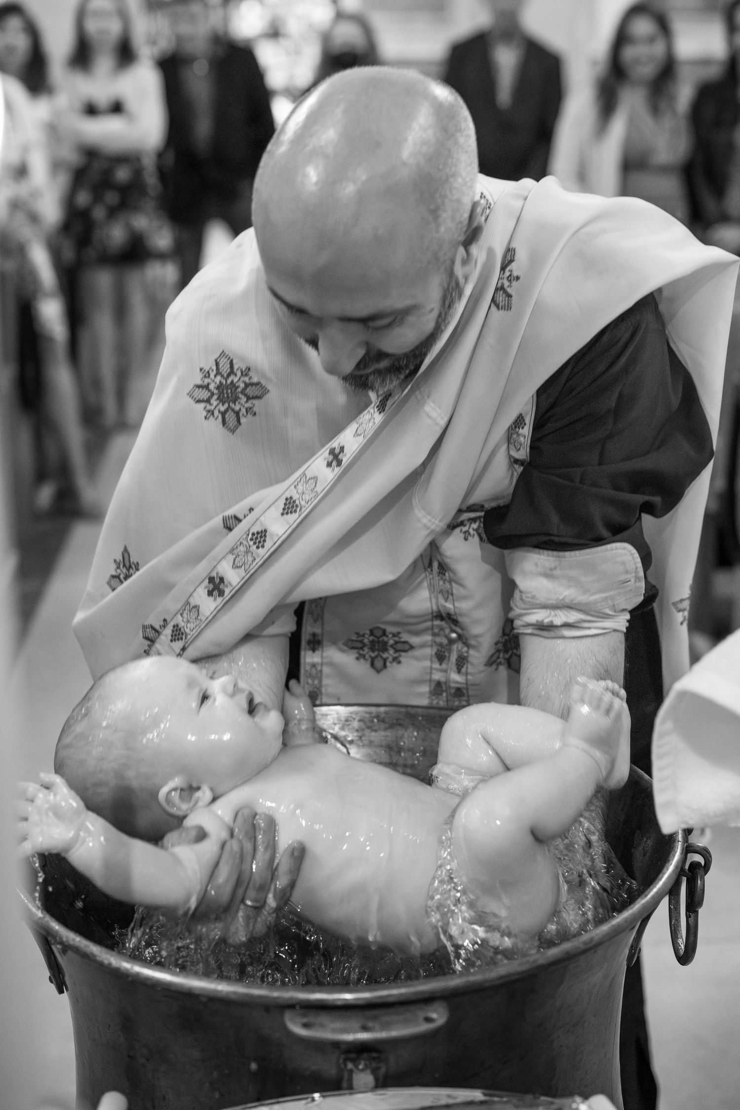 A religious baptism ceremony showing a priest performing the ritual with a baby in white robes.