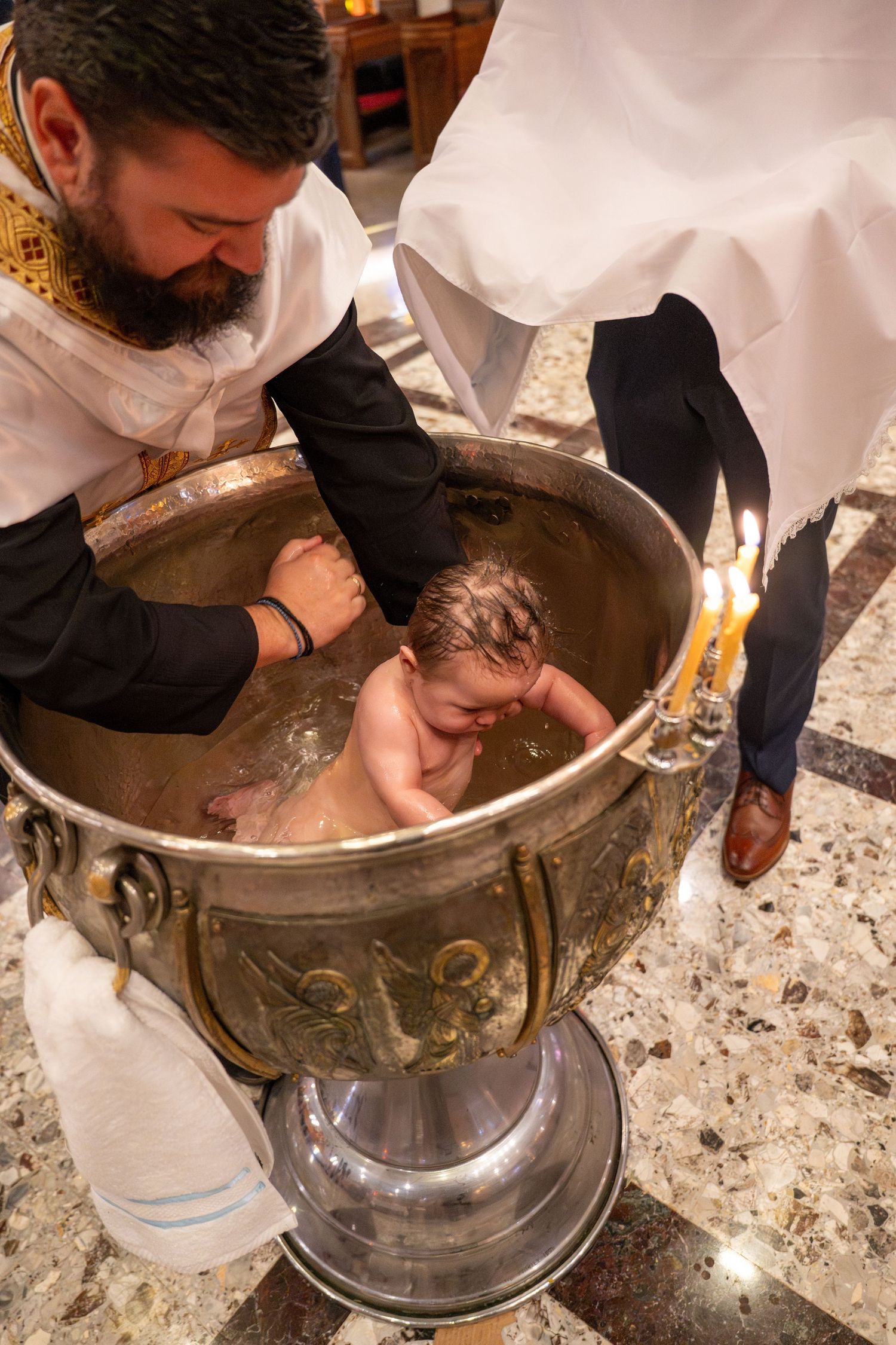 Close-up of baptism ritual being performed in decorated metal font.