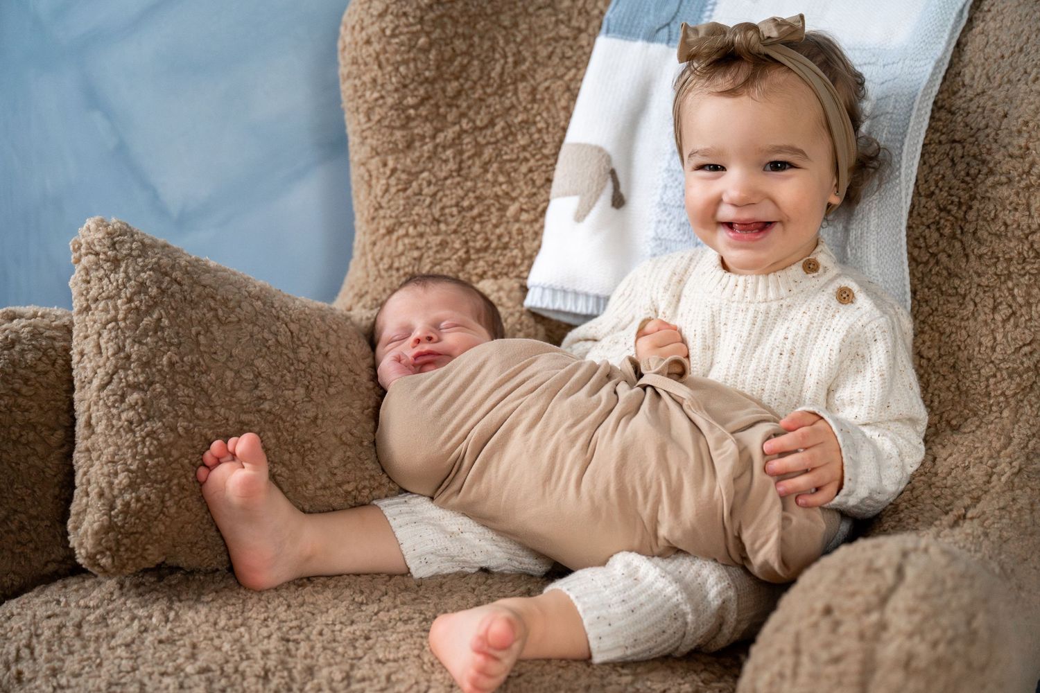 A smiling baby wearing a white sweater lies on a beige couch in a series of candid photos.