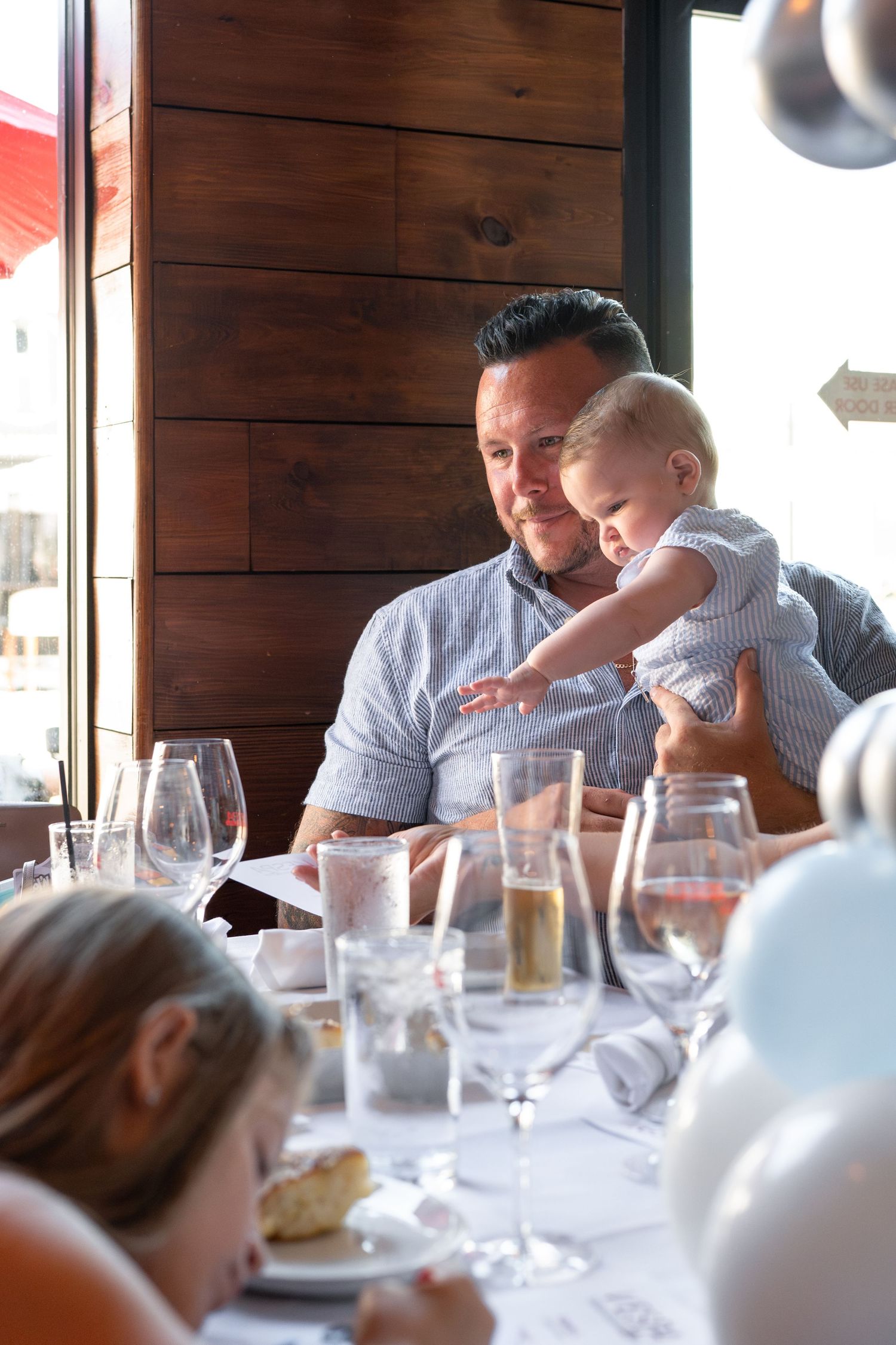 A family gathering at a restaurant with wood paneled walls and table settings with wine glasses.