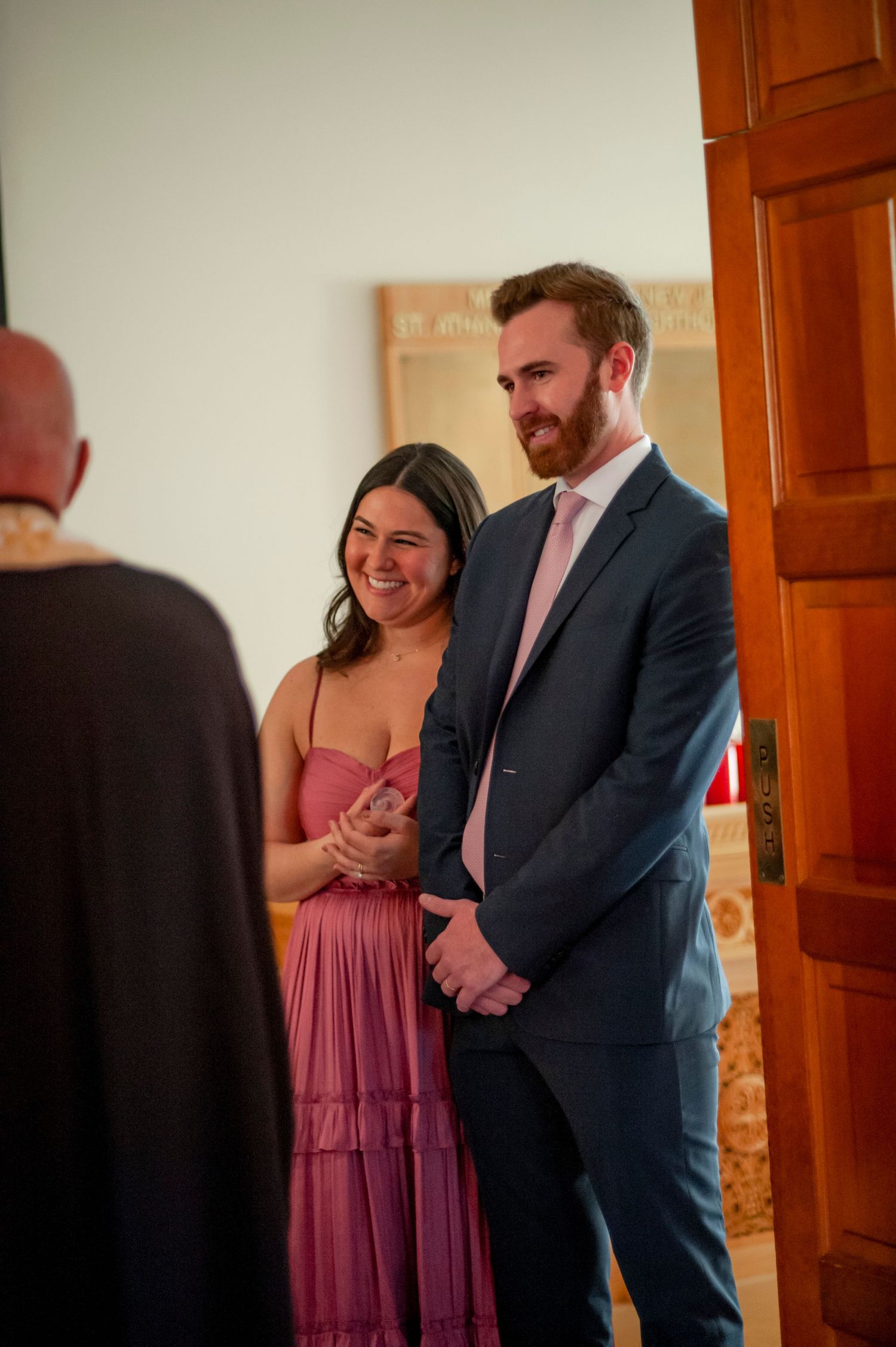 A couple in formal attire shares an emotional moment in a doorway, with the woman in a mauve dress and man in a suit.