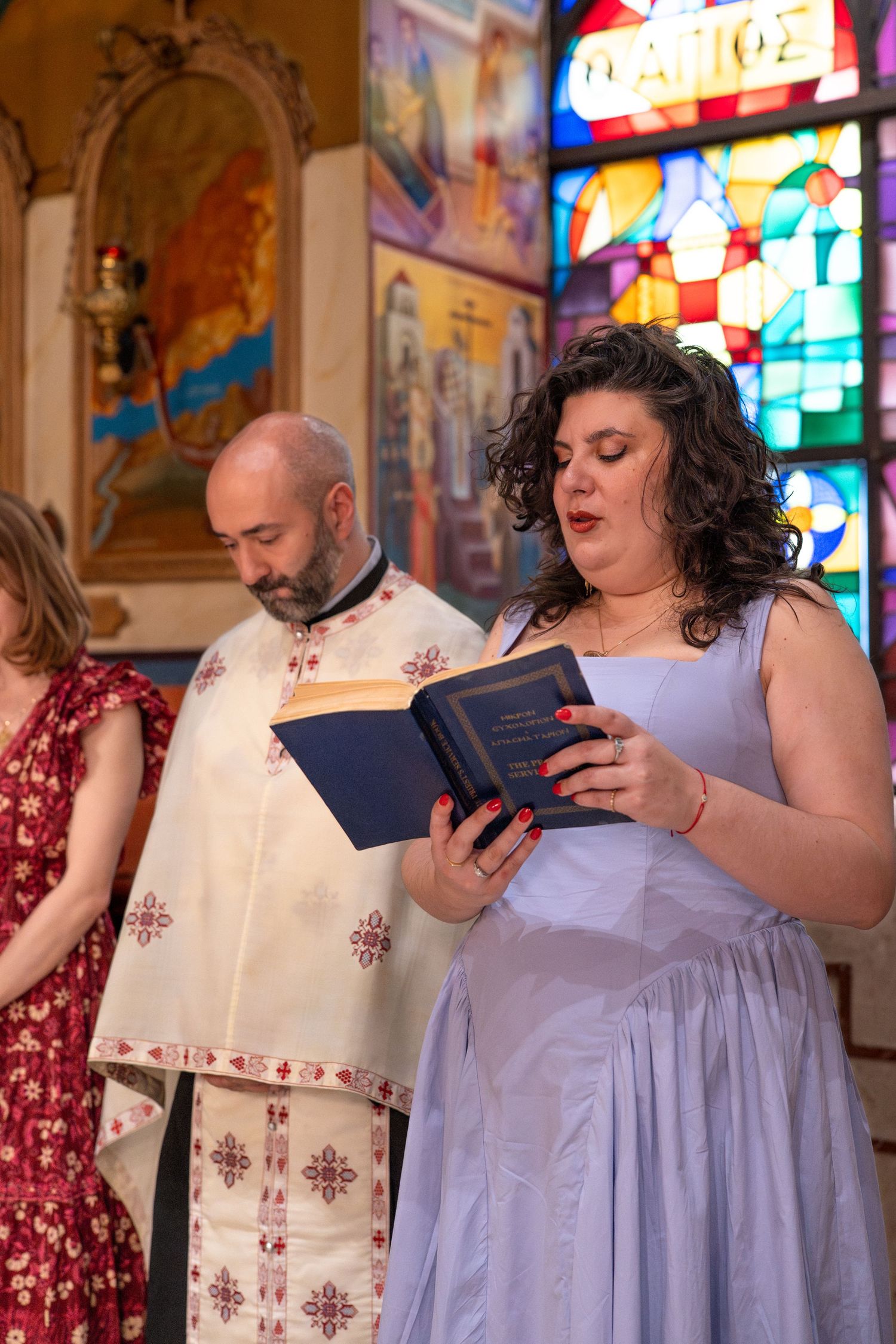 People in formal attire reading from prayer books during a religious ceremony in a church.