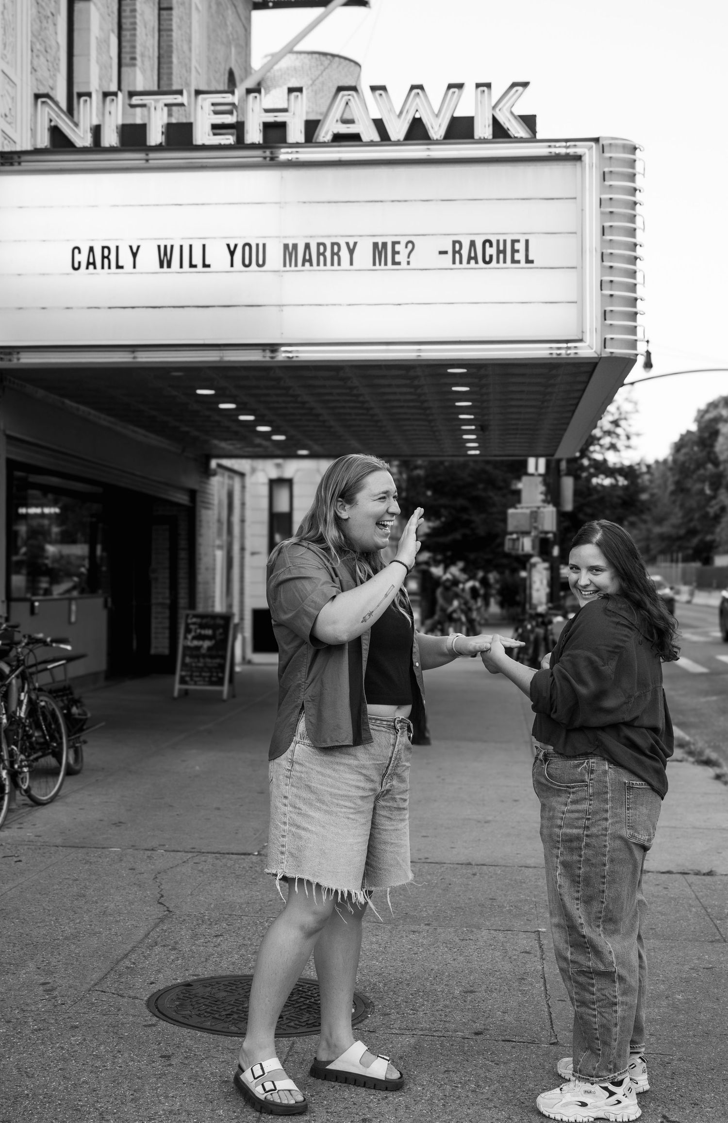 A black and white photo shows a movie theater marquee with a marriage proposal message outside the Nitehawk Cinema.