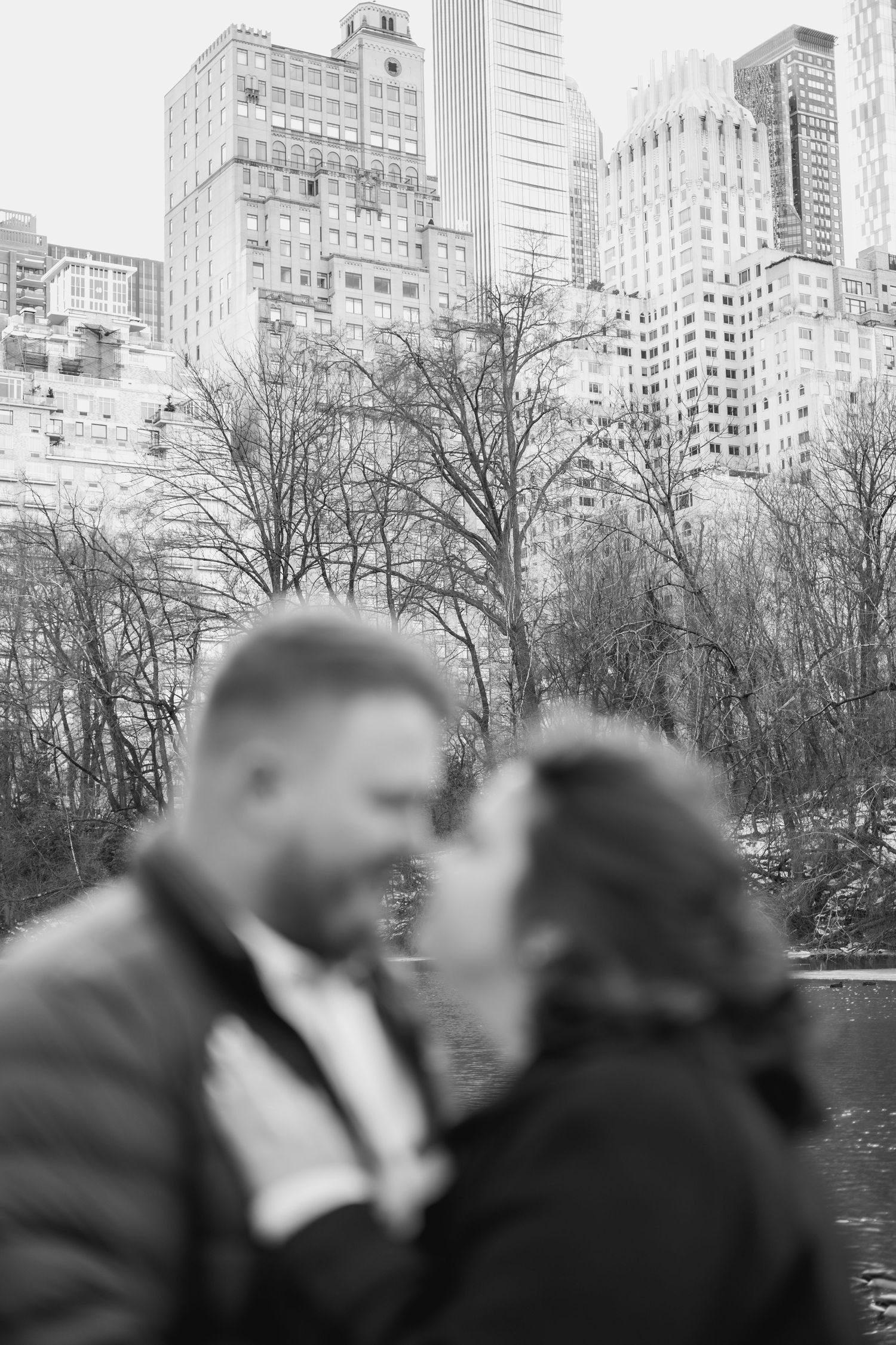Silhouetted couple sharing a romantic kiss with Manhattan skyline and Central Park lake in the background.