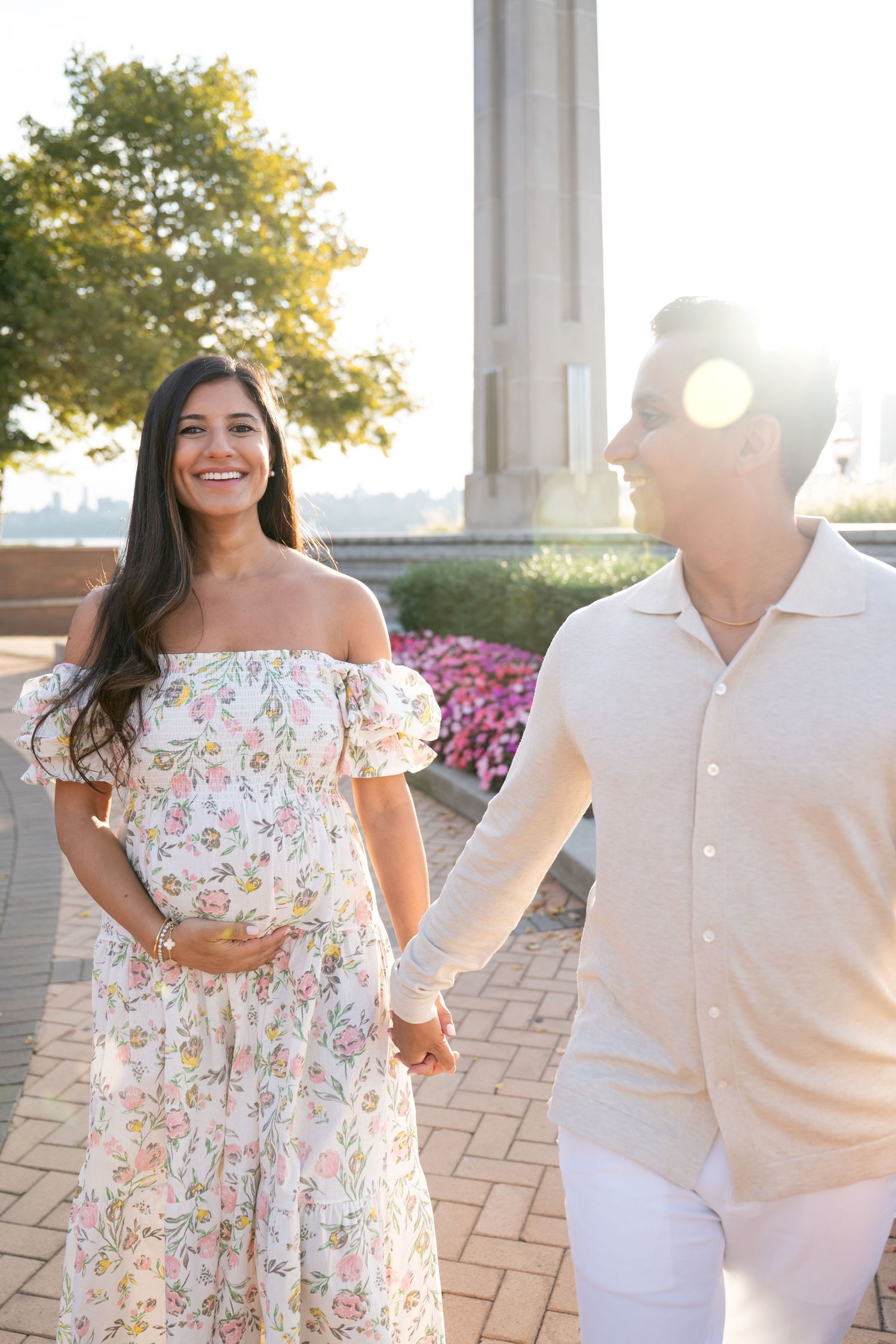Couple in floral dress and white outfit laugh together during sunset photoshoot.