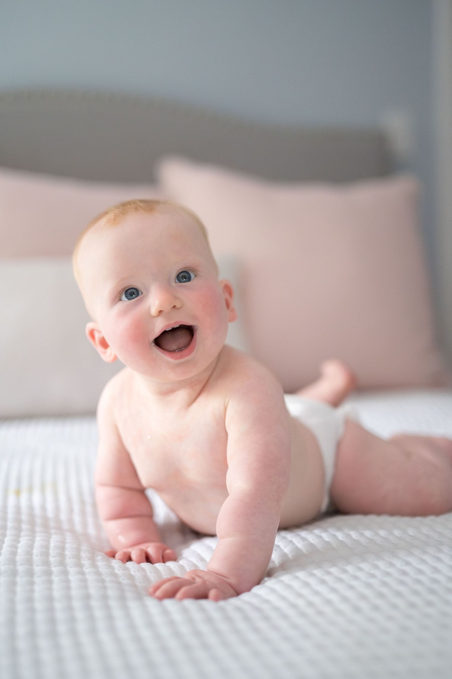 A smiling baby lying on white bedding showing different poses and expressions during a photo session.