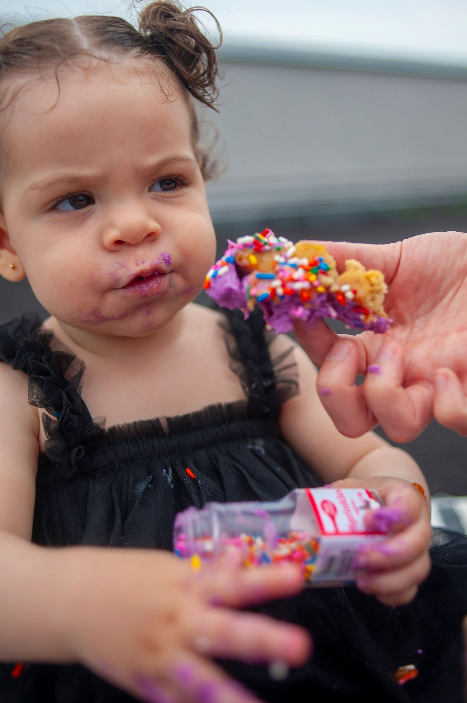 Child in black dress holding colorful confetti and treats.