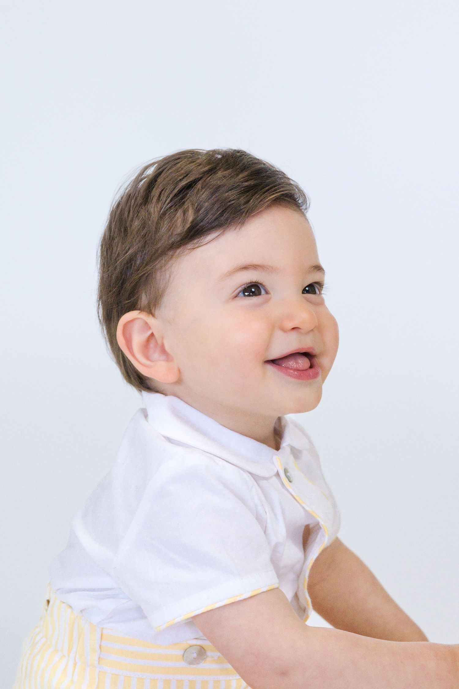 Baby in white outfit smiling and looking up against white studio background.