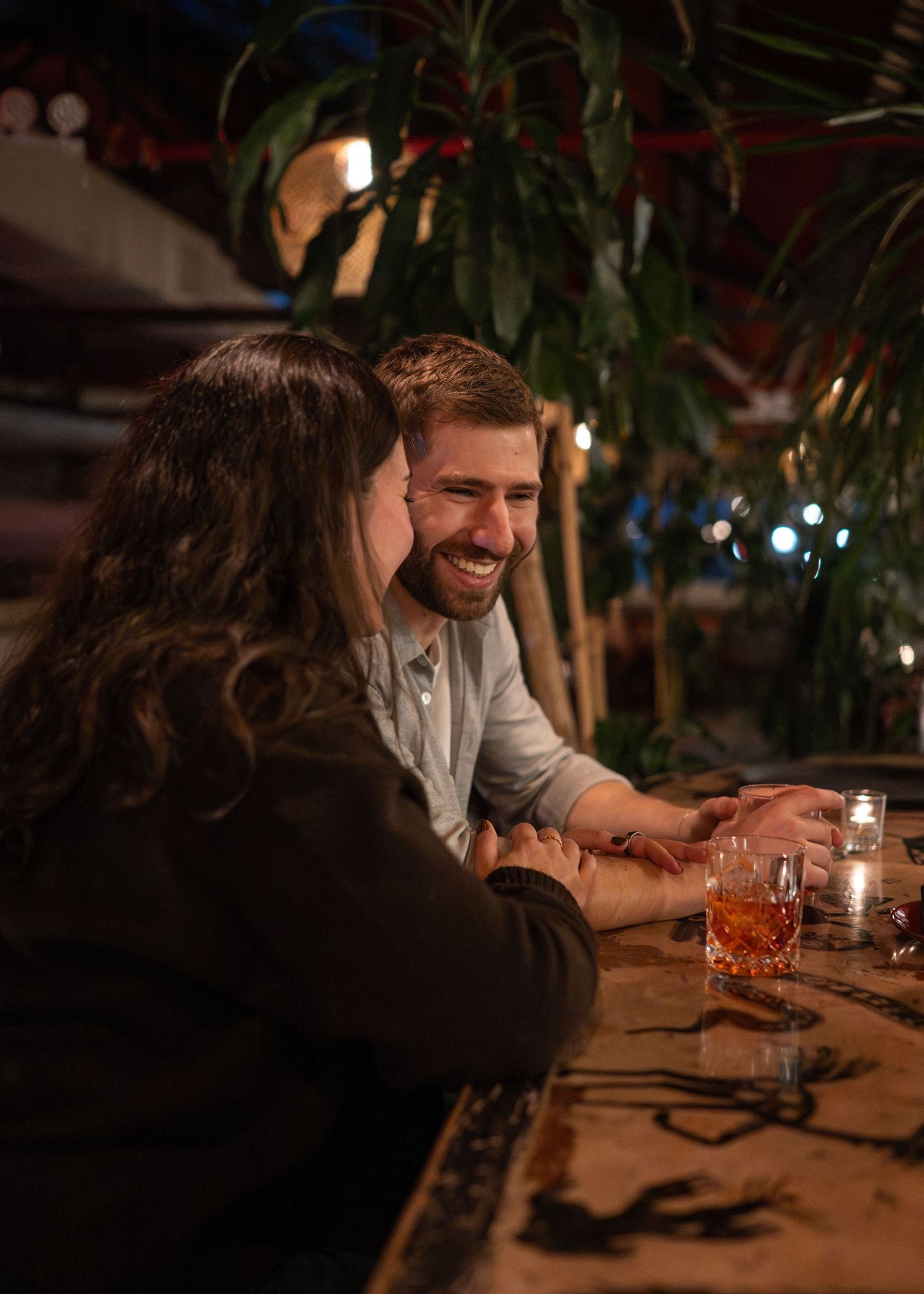 Friends gathered around a candlelit table with drinks in a cozy restaurant setting.