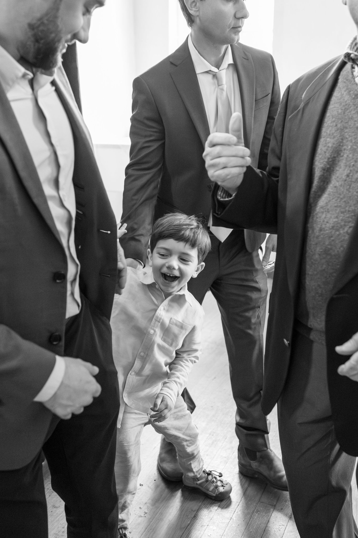 Young boy in white traditional outfit smiling among adults in suits at a formal event.