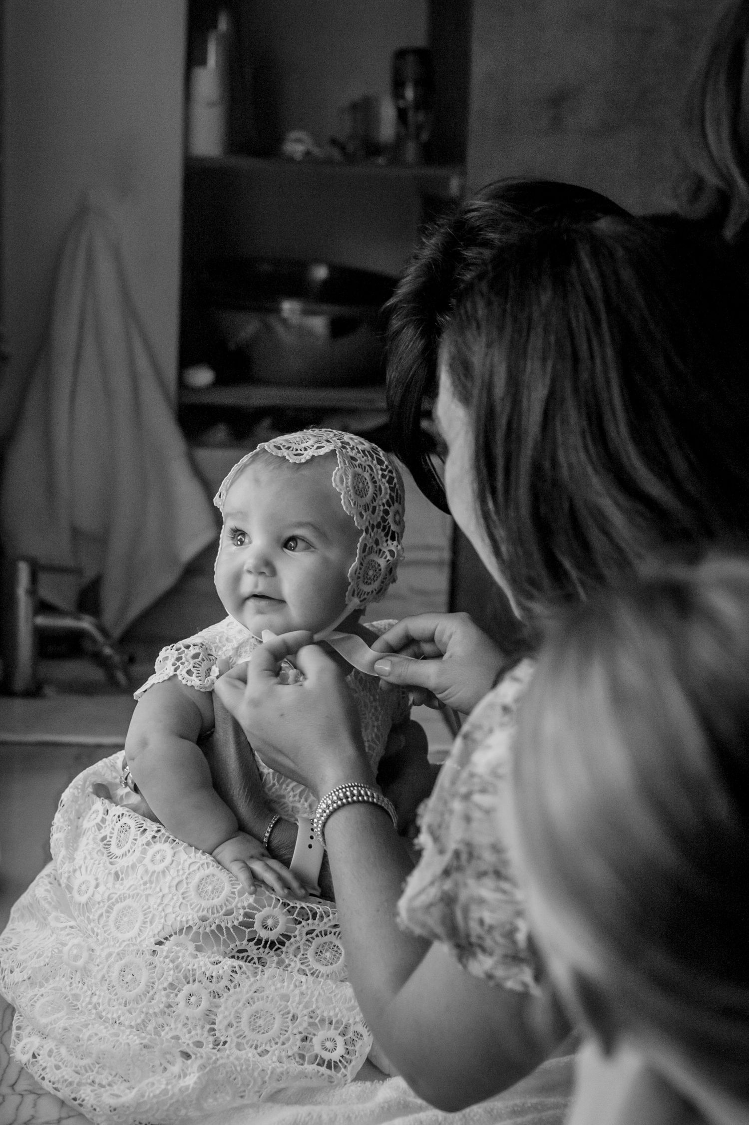 Series of black and white photos showing tender moments between woman and baby in white lace dress.