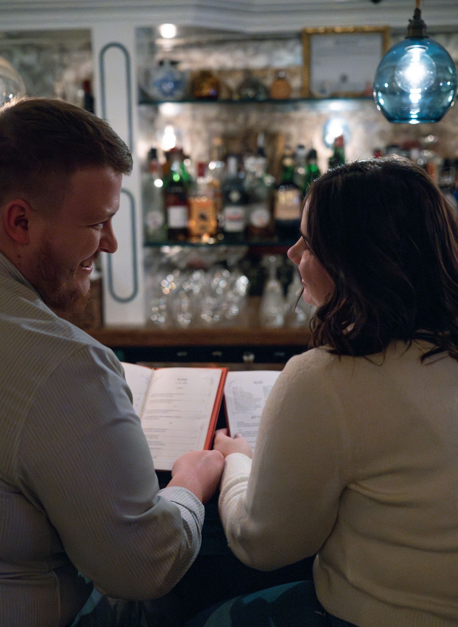 A couple sits at a bar counter reviewing menus in a dimly lit restaurant setting.