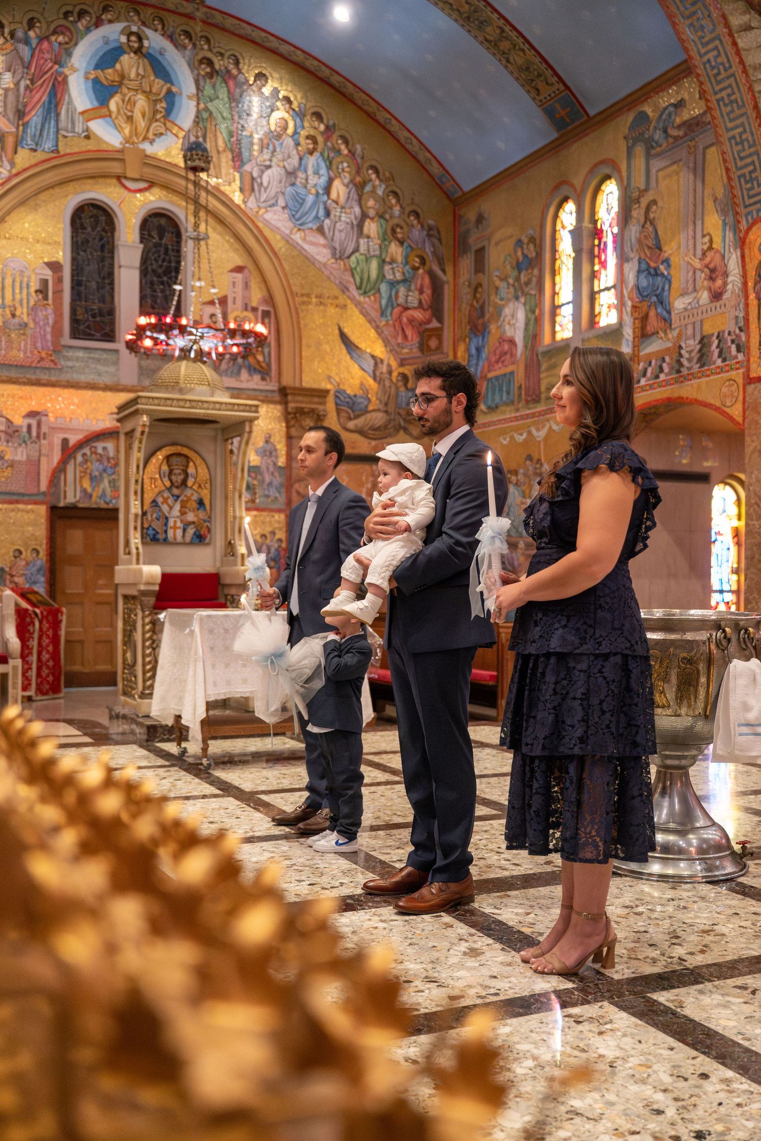 A panoramic view of a baptism ceremony in a beautifully decorated church with painted murals and arched ceilings.