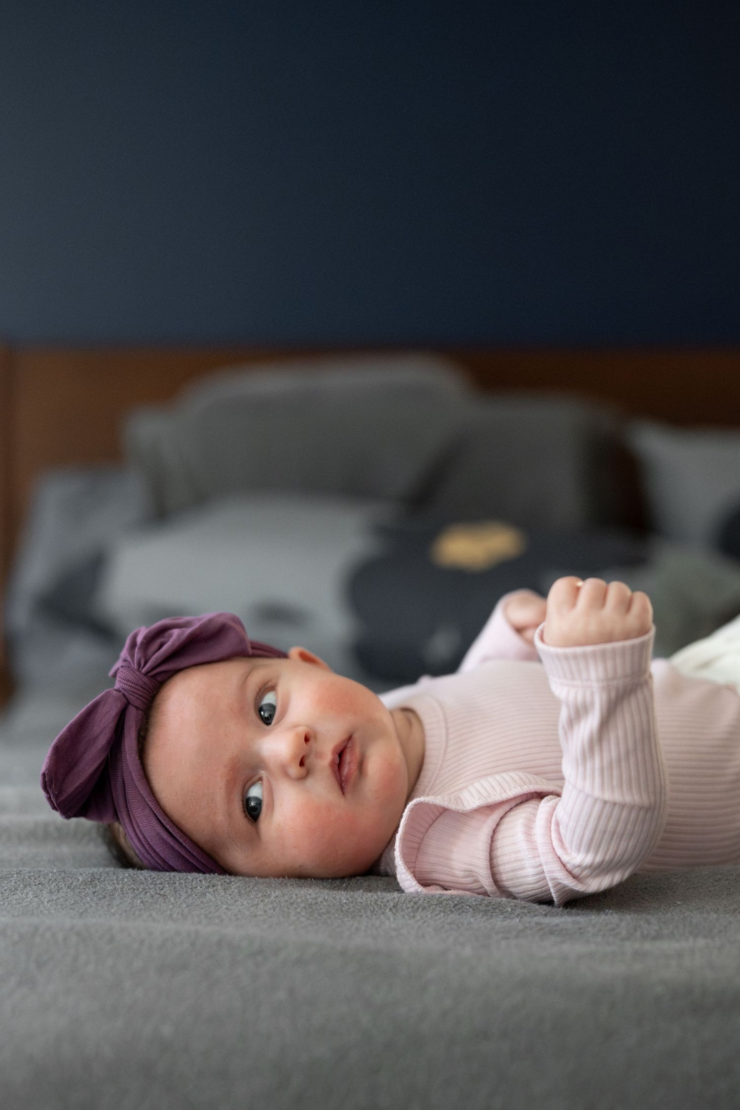 Baby in pink sweater and purple headband lying on grey surface, photographed from above.