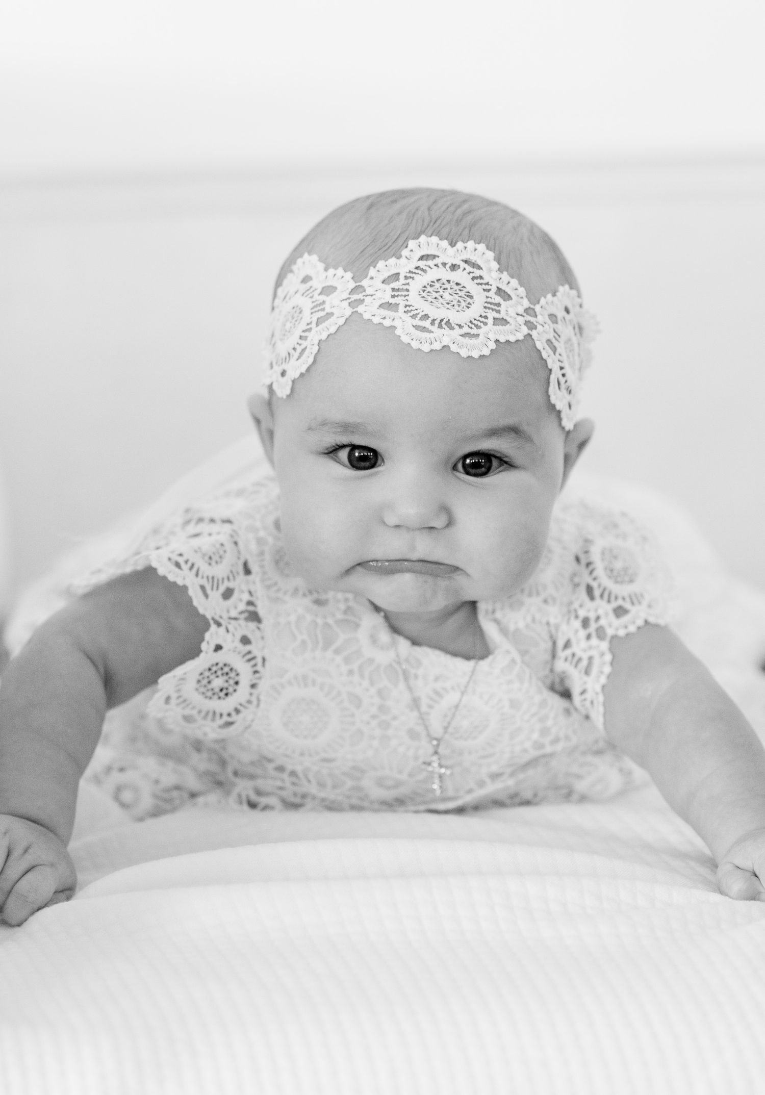 Black and white portrait of baby in lace outfit on white background.