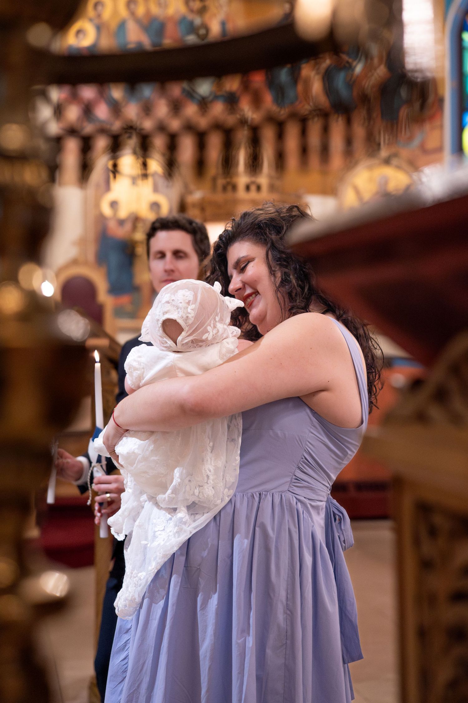 People in formal attire gather for a baptism ceremony in a decorated church interior.