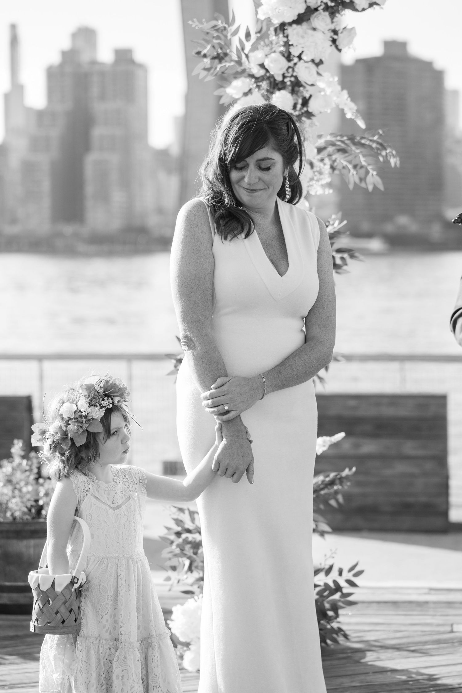 A romantic black and white wedding moment captured at a waterfront venue with city skyline in the background.