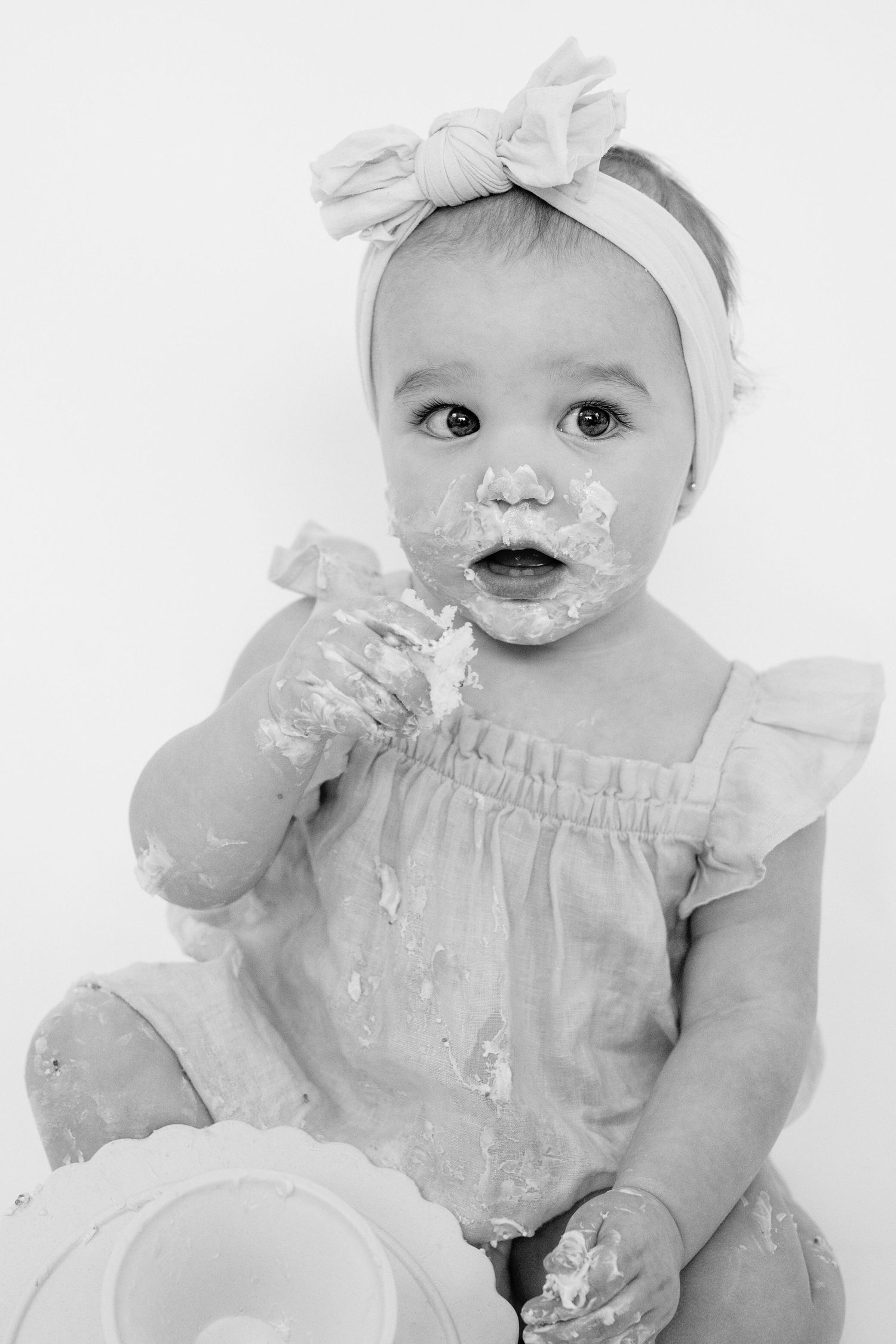 Black and white portrait of messy baby in dress with bow headband.