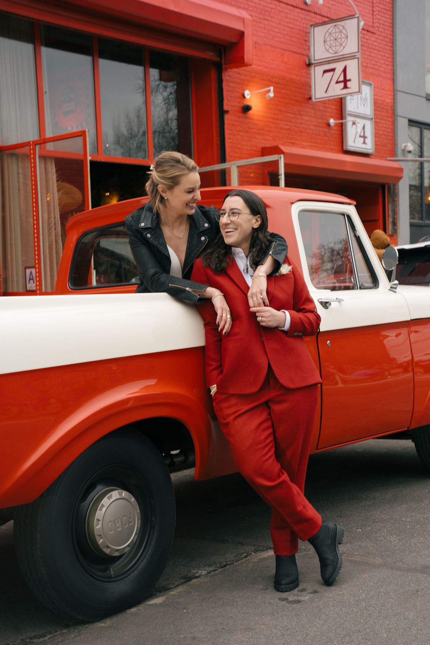 Couple posing playfully next to vintage red and white car.