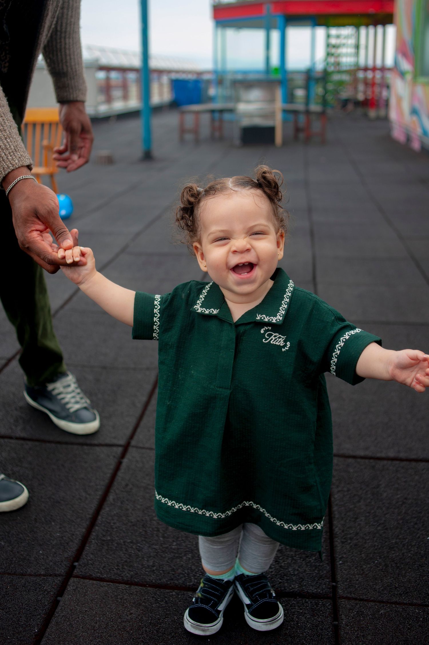Child in green uniform dress playing on outdoor playground.