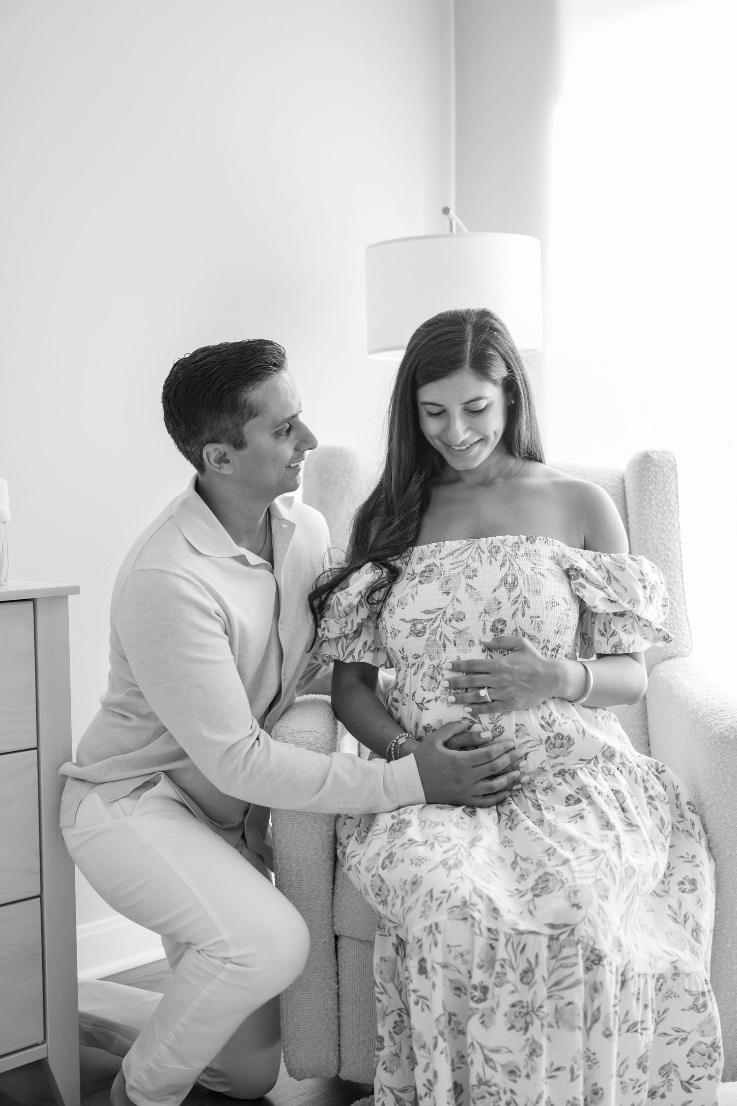 Black and white photo of a couple in light colored outfits sharing a tender moment on a chair.