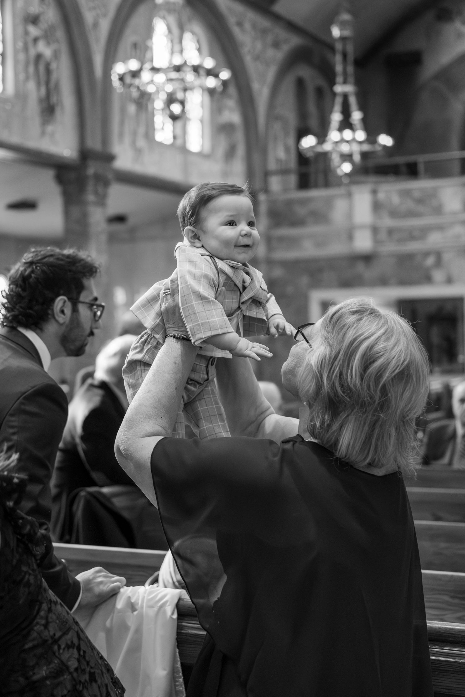 Black and white photo of people lifting babies during a church ceremony.