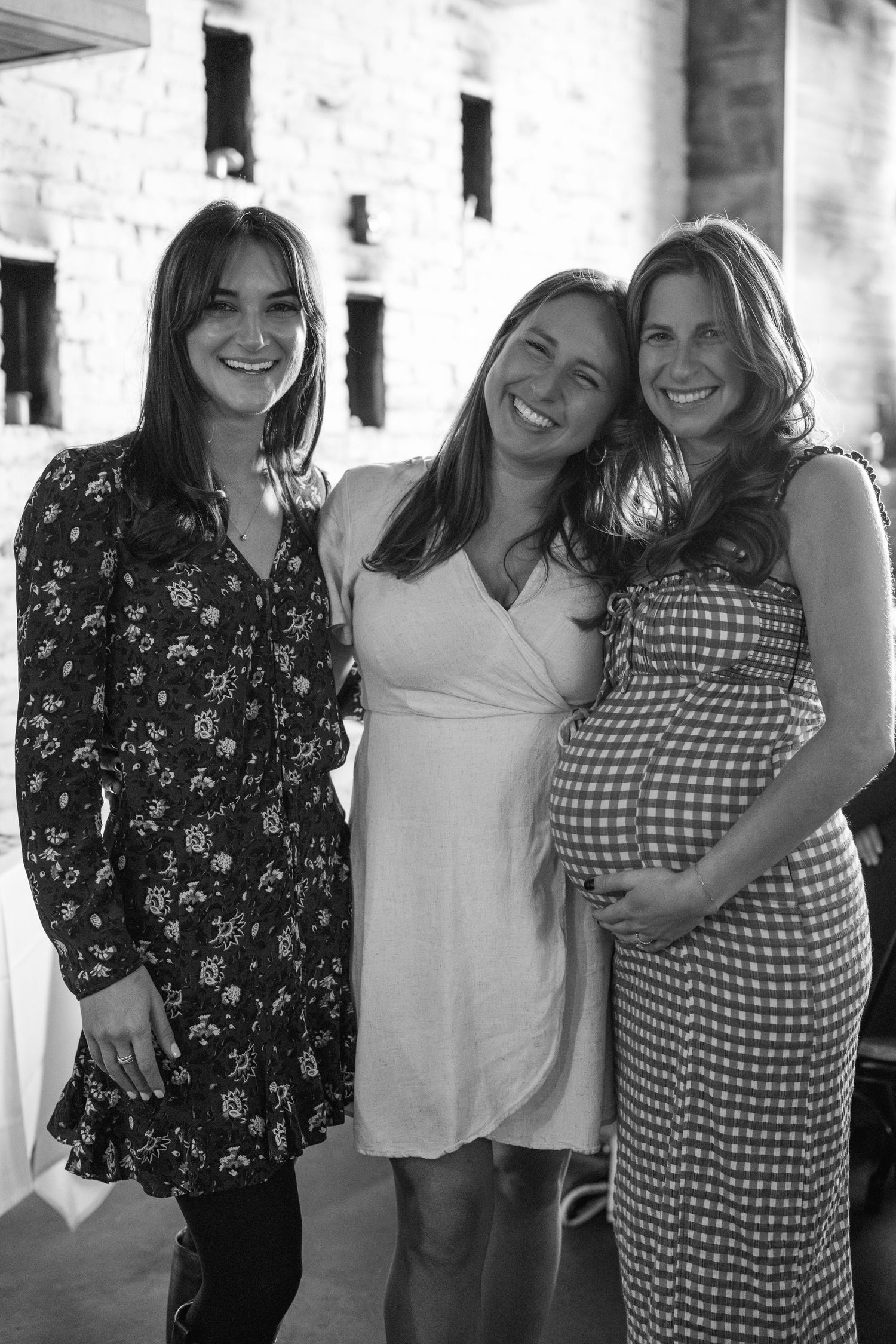 Friends in floral and gingham dresses posing together against a white brick wall.