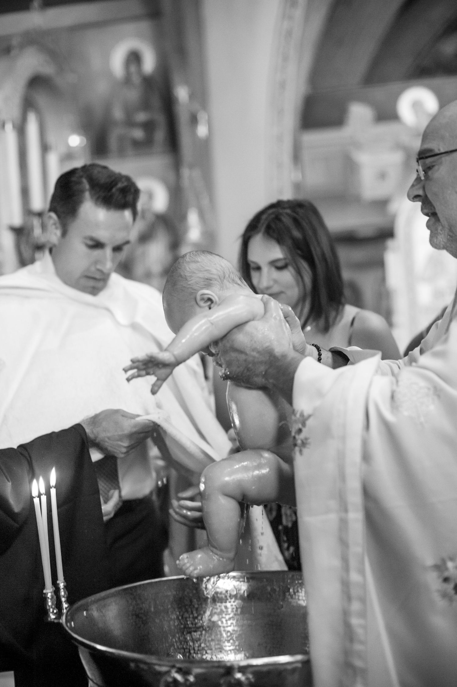 Clergy members performing a religious baptism ceremony around an ornate silver font.