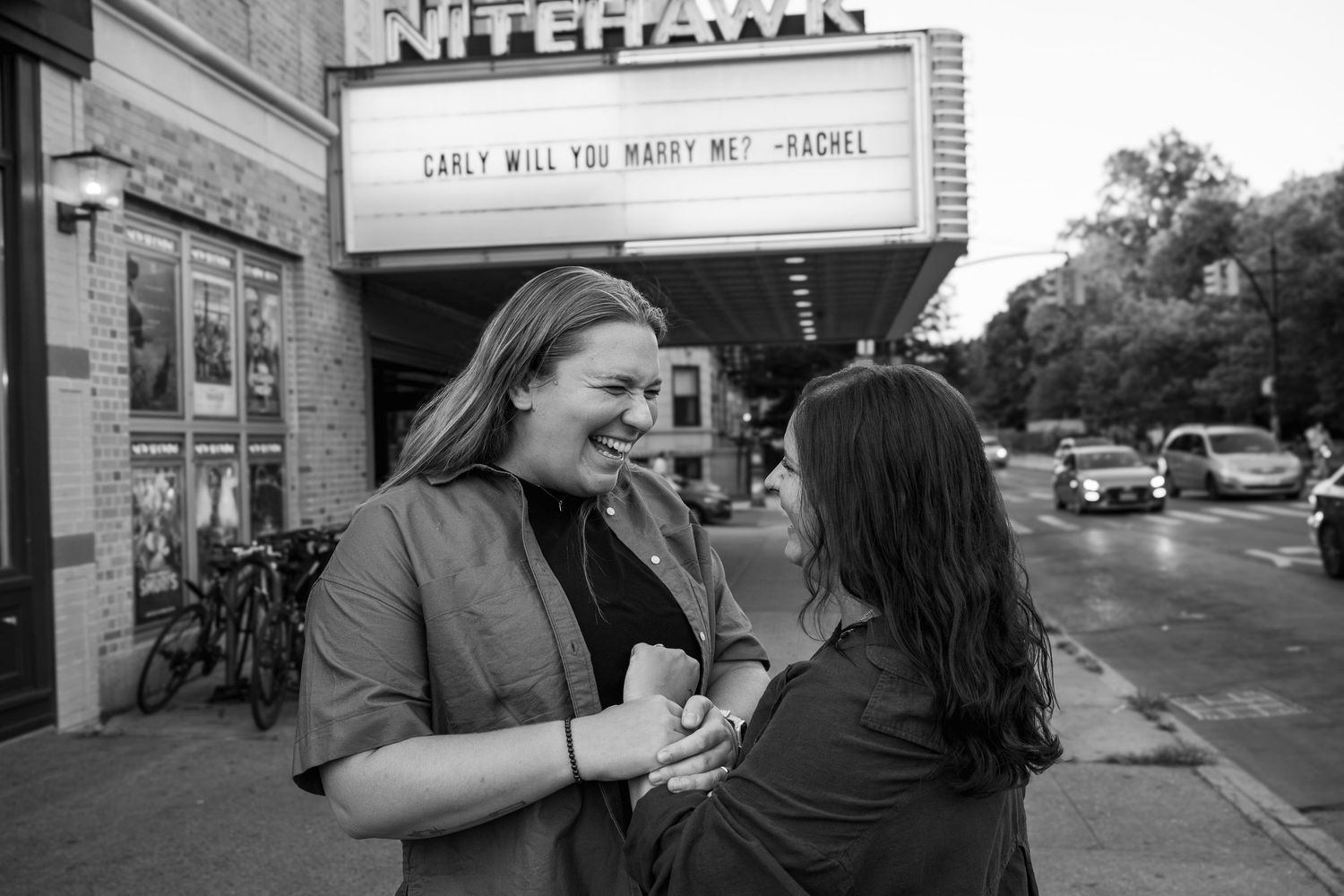 People sharing a warm embrace and laughing together in front of a brick building.