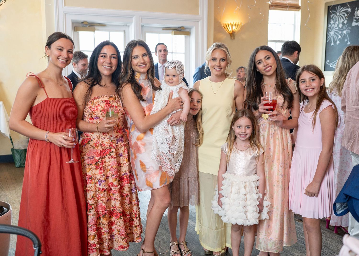 Group of women and girls in colorful dresses posing together at an elegant indoor celebration or party.