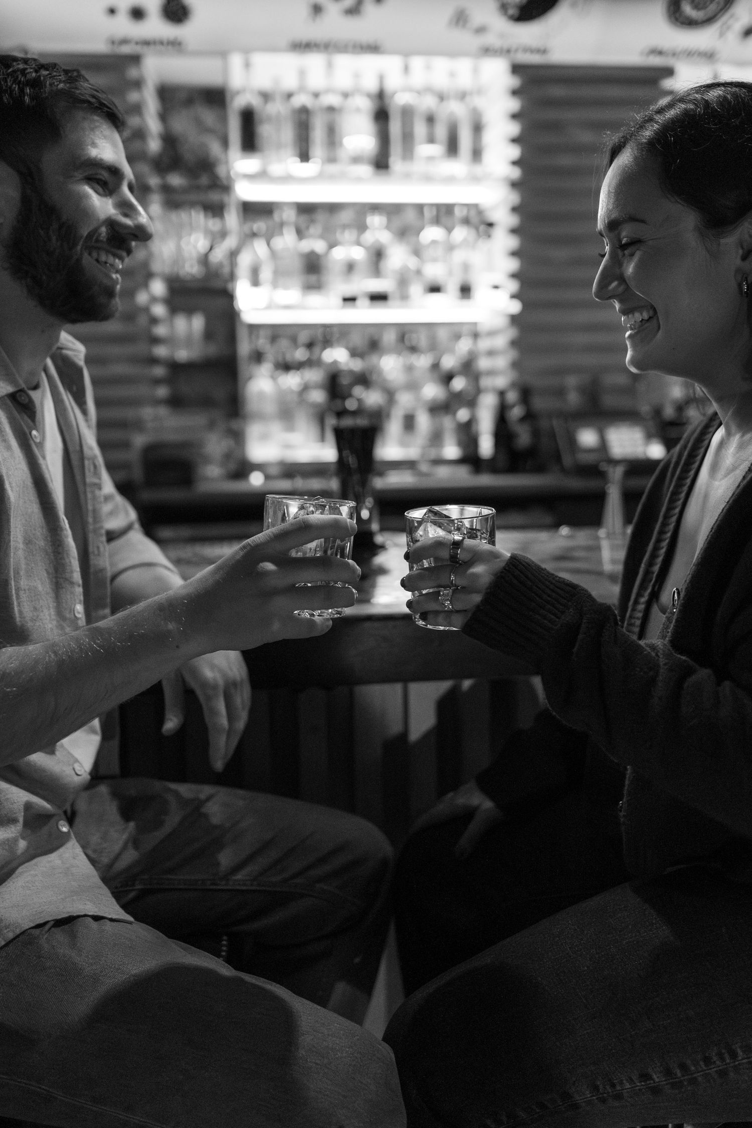 Black and white photo showing people enjoying drinks and conversation at a dimly lit bar counter.