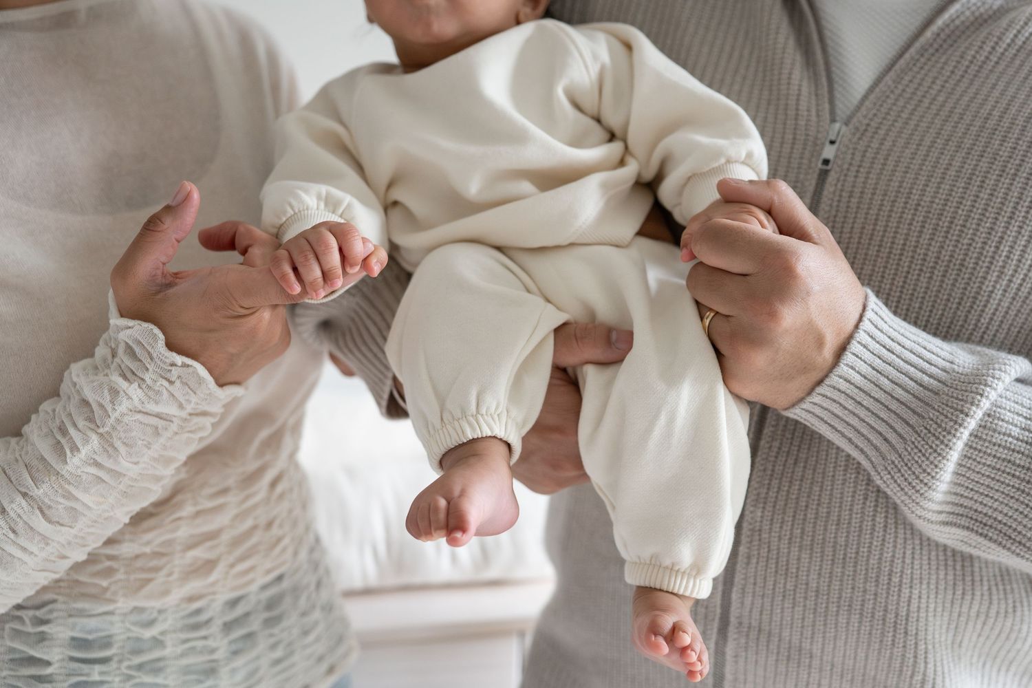 A collection of photos showing a baby in white clothing being held against a gray background.