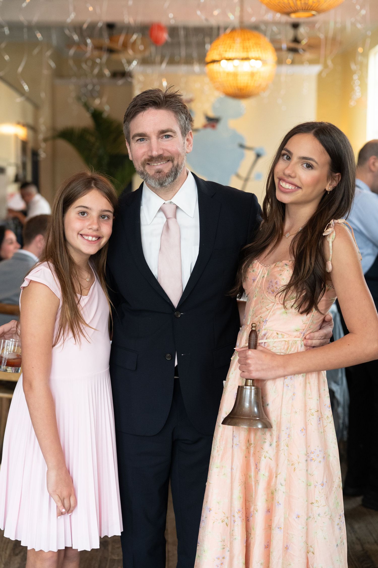 A man in a suit poses with two young women in elegant dresses at a formal event.