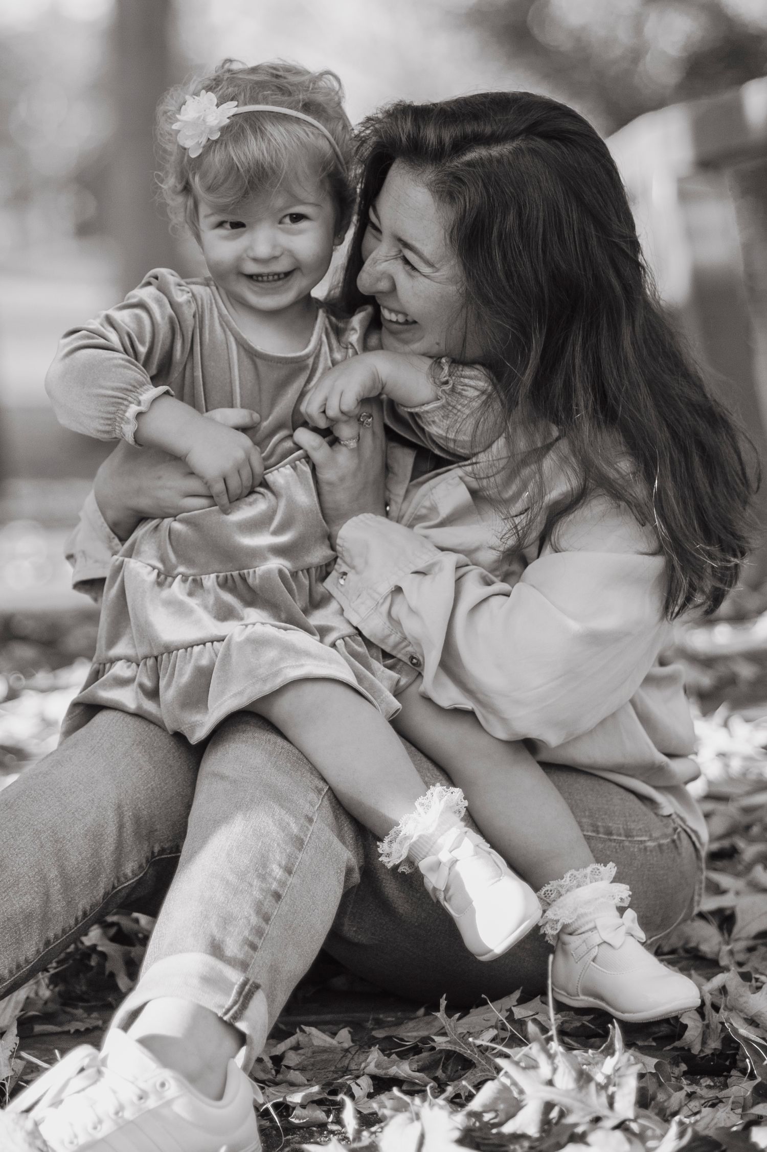 Black and white photos capturing joyful moments between parent and child sitting in fallen leaves.