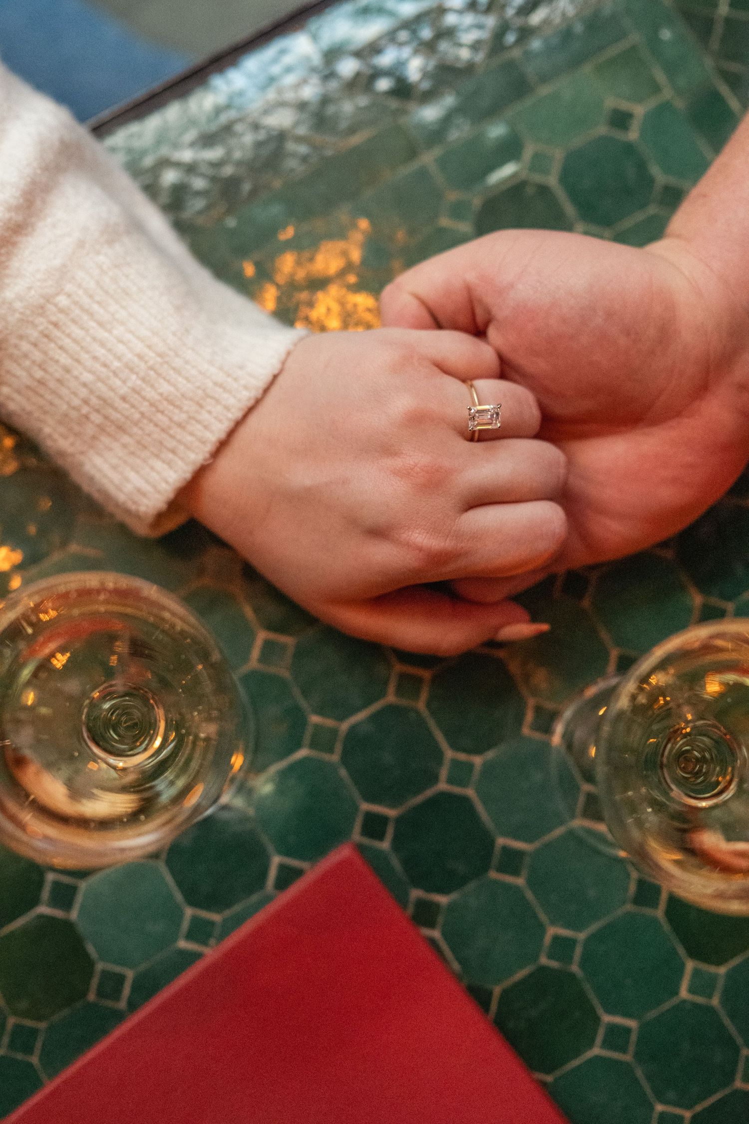 Close-up of hands with wedding rings resting on a decorative green table surface with candlelight.