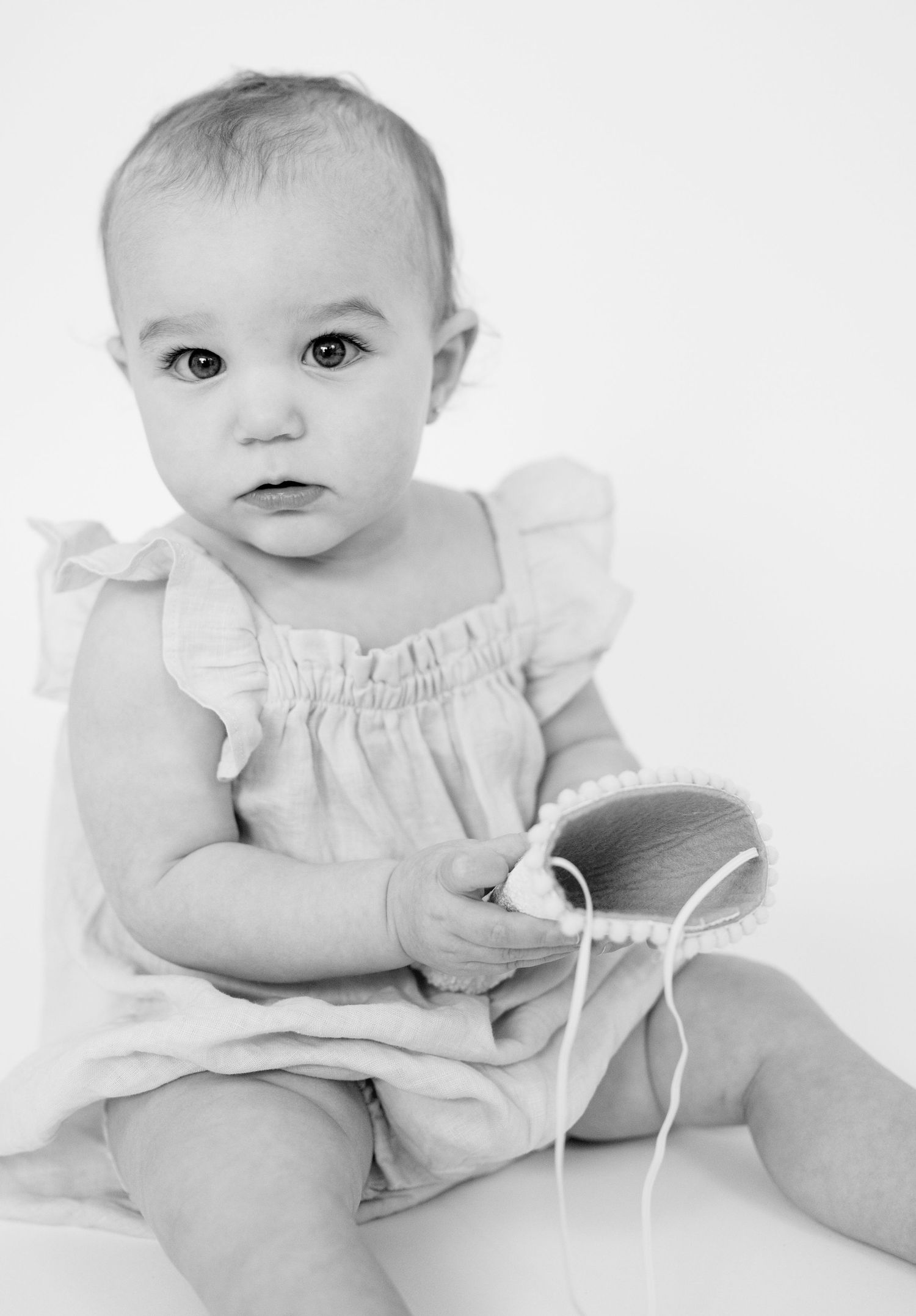 Black and white portrait series of a baby wearing a white ruffled outfit against a light background.