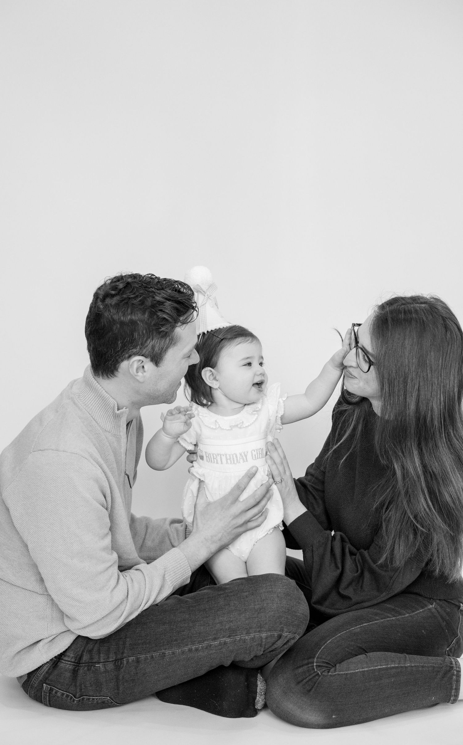 Black and white family photo showing parents playing with baby on floor.