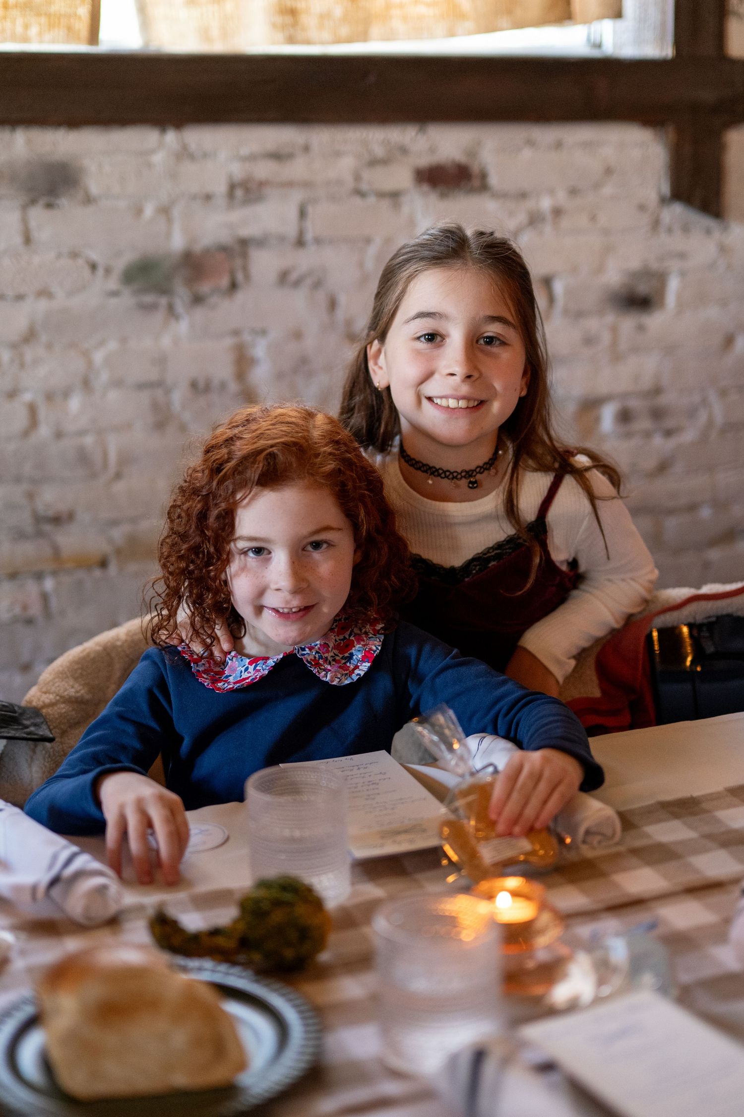 Children enjoying a meal together at a restaurant table with candlelight and brick wall backdrop.