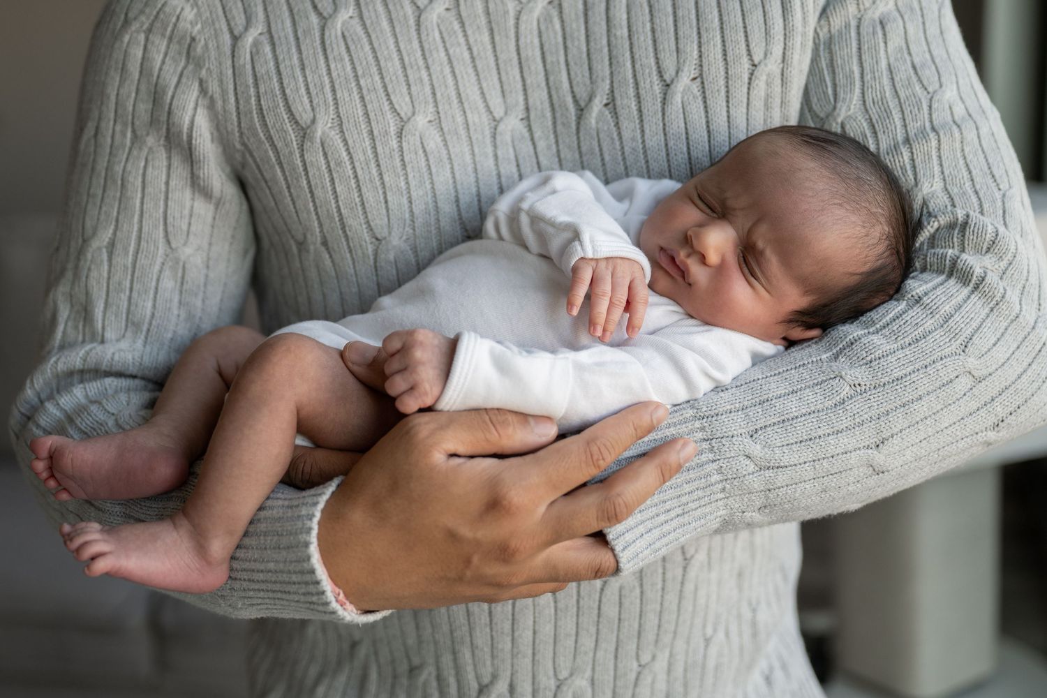 Gentle moments with a newborn wearing a light-colored outfit against a gray sweater.