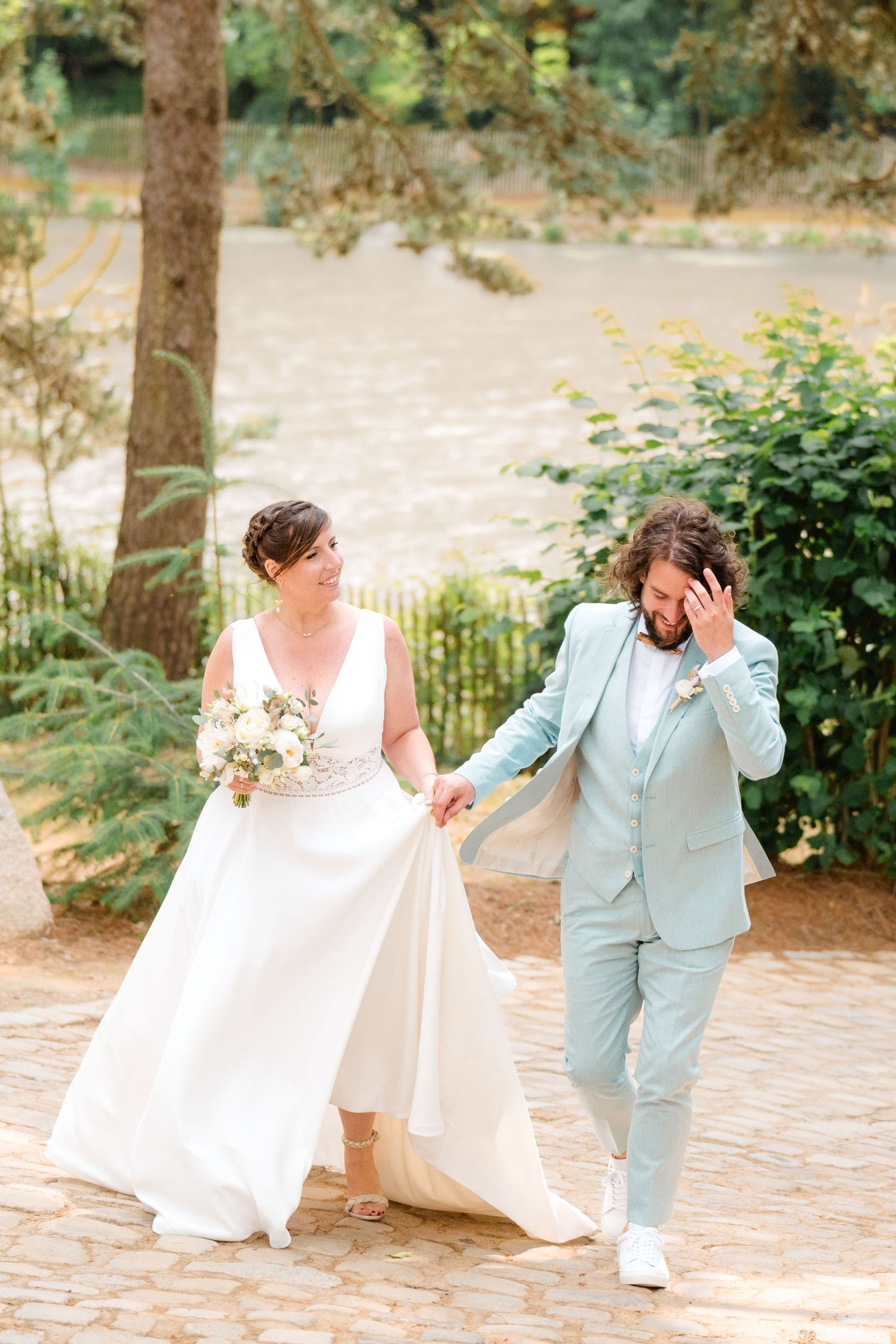 Mariés complices marchant main dans la main au domaine les 3 rivages, robe fluide et costume vert pastel, reportage mariage à Nantes.