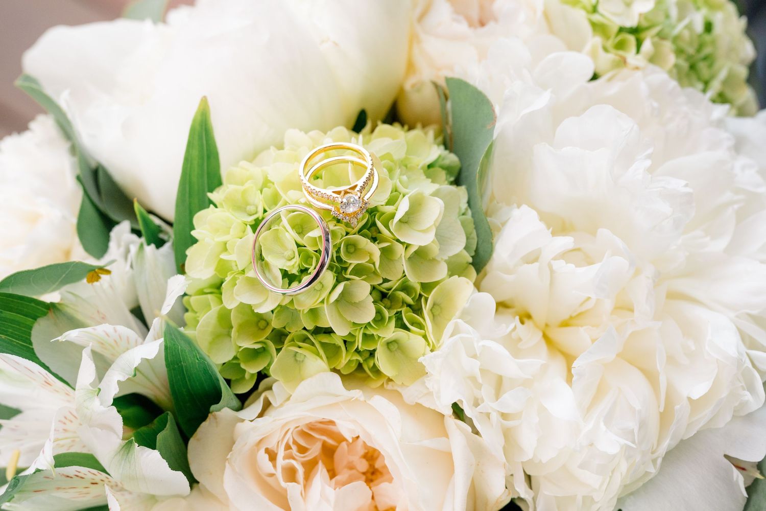 Un magnifique bouquet de mariage composé de pivoines blanches, de roses crème et d’hortensias vert clair, agrémenté d’un délicat feuillage.
