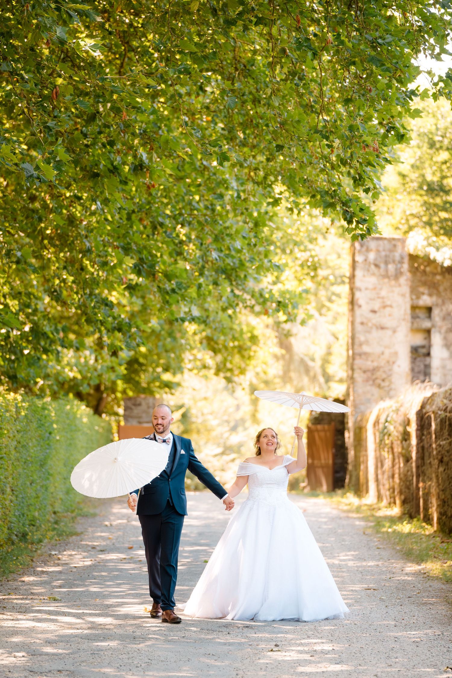 Mariés élégants marchant dans une allée arborée, ambiance romantique et naturelle au château haute goulaine – photographe mariage Nantes.