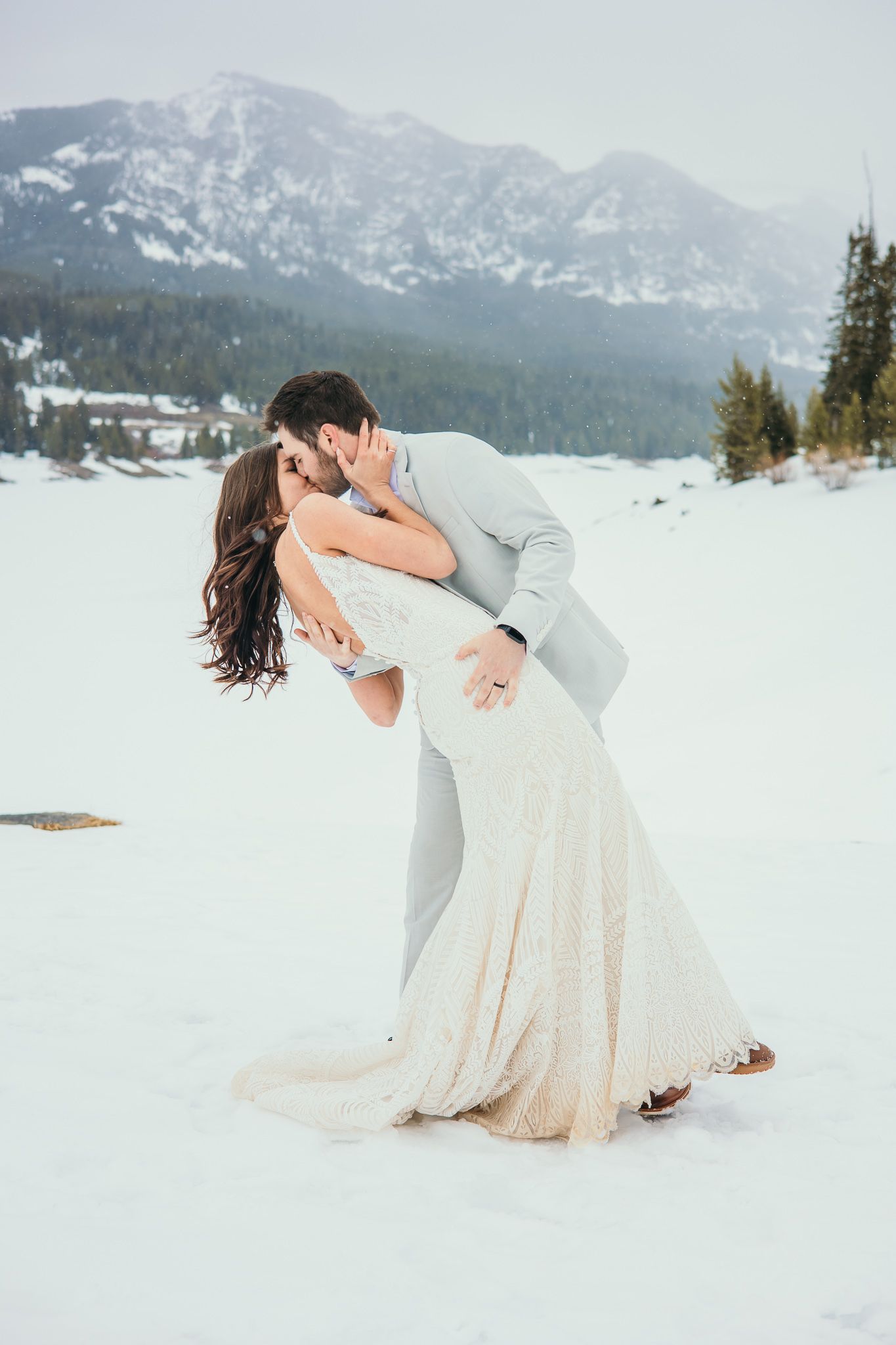 Dramatic wedding dip pose photographed in snowy mountain landscape.