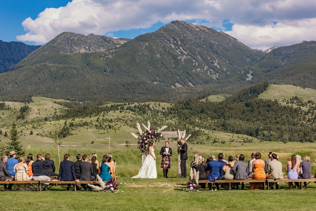 Wedding ceremony setup with wooden benches and mountain backdrop in natural setting.