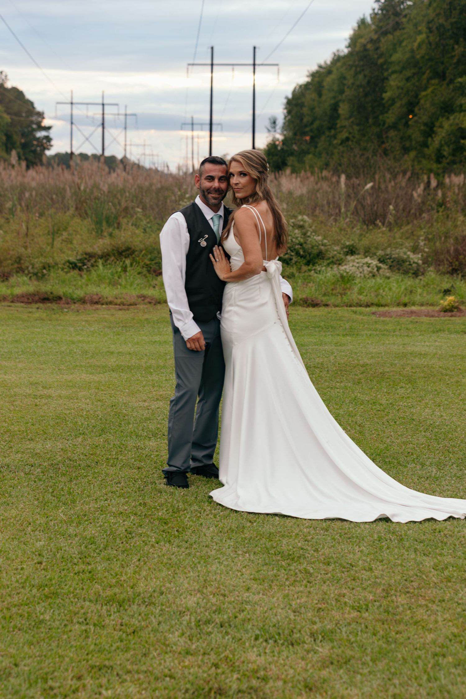 Wedding couple embracing in an outdoor field with long white dress train.