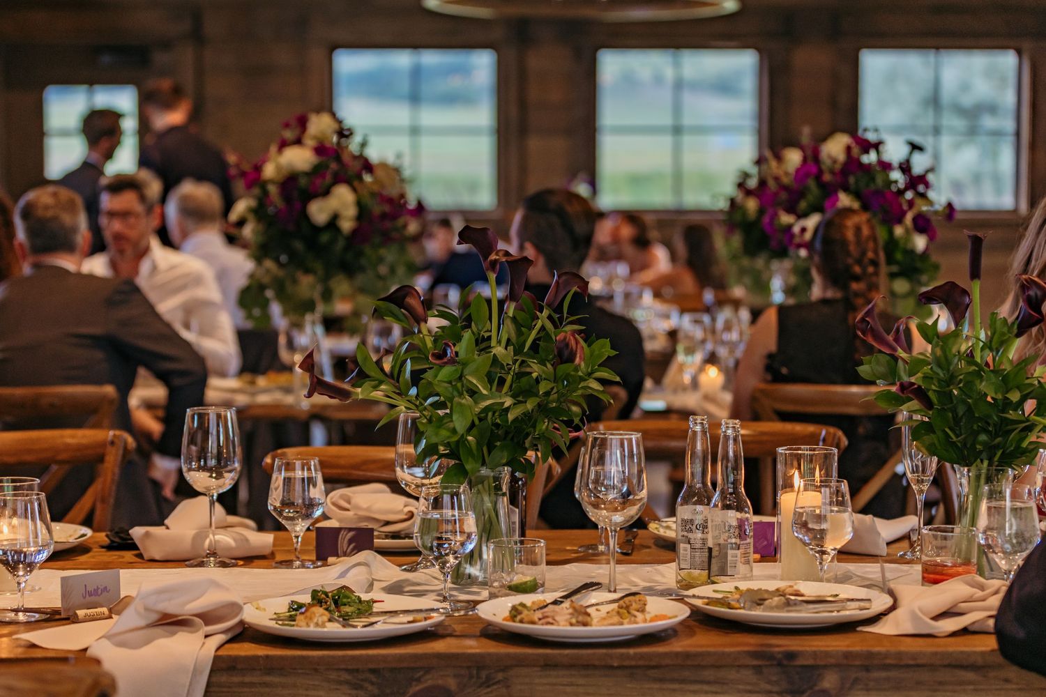 Elegant wedding reception table setting with floral centerpieces and place settings in a rustic venue.