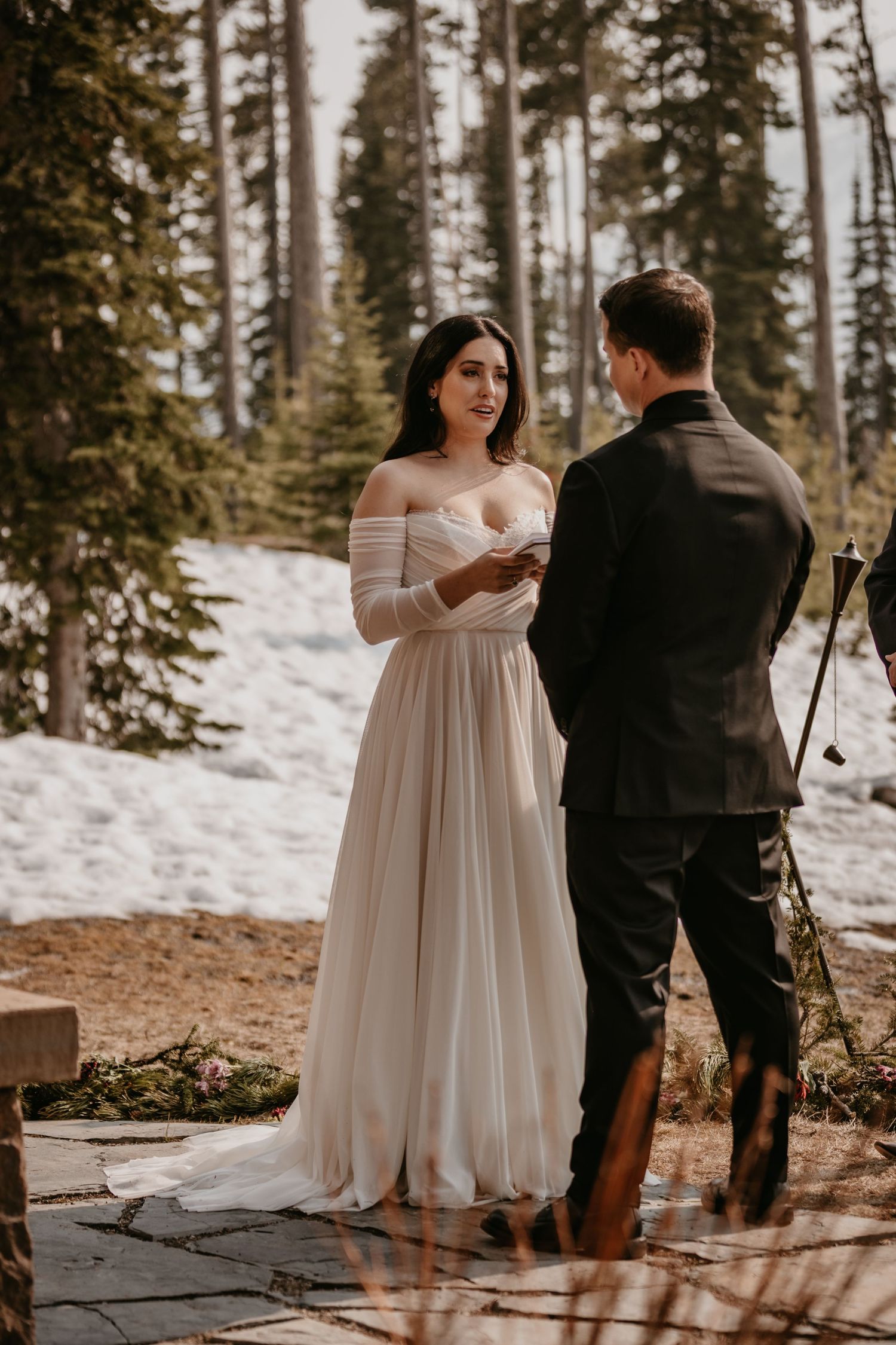 A romantic winter elopement scene with a bride in a flowing white dress against a snowy mountain backdrop.