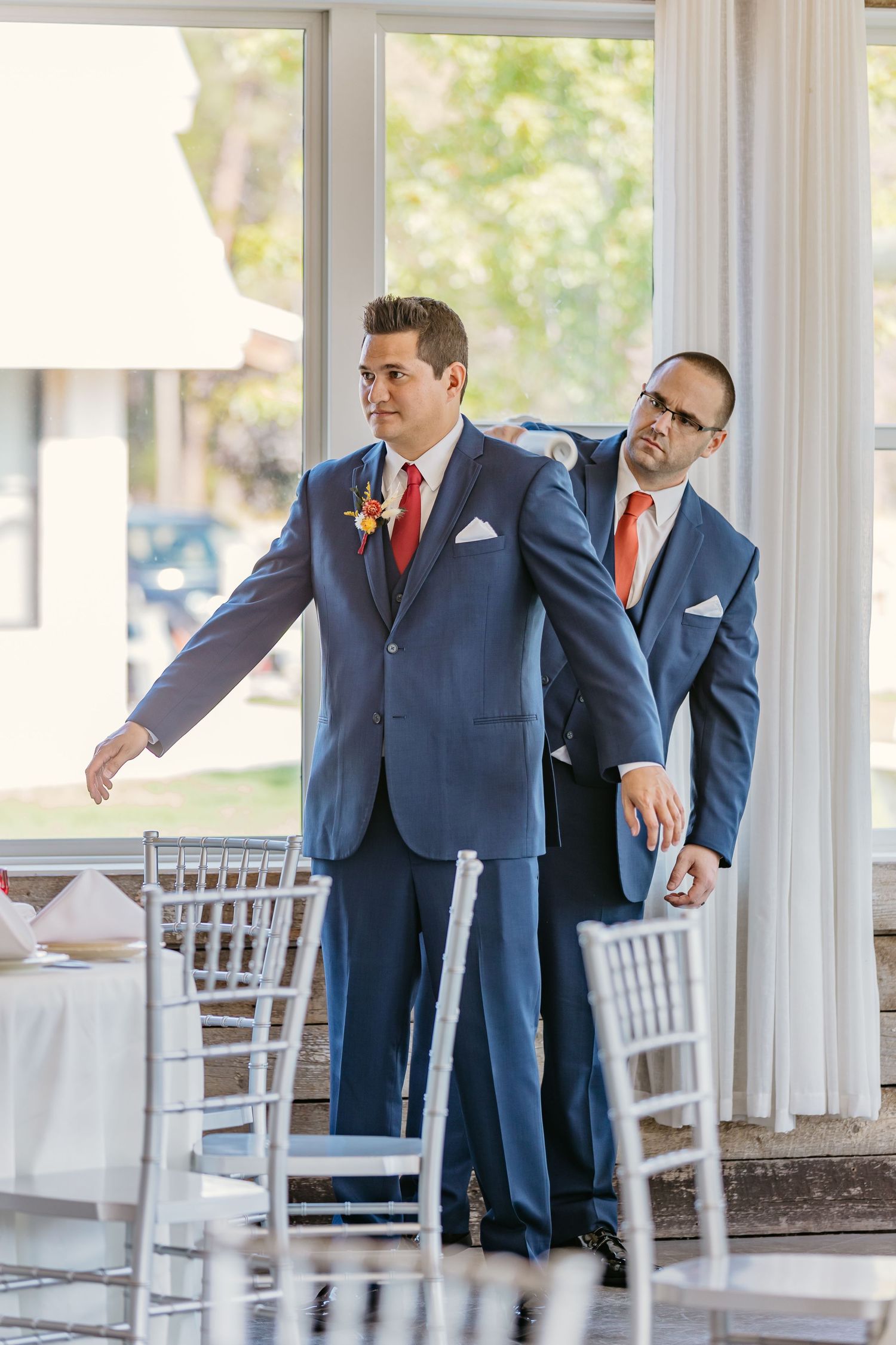 Groomsmen in navy suits practice dance moves in a bright venue with white chairs.