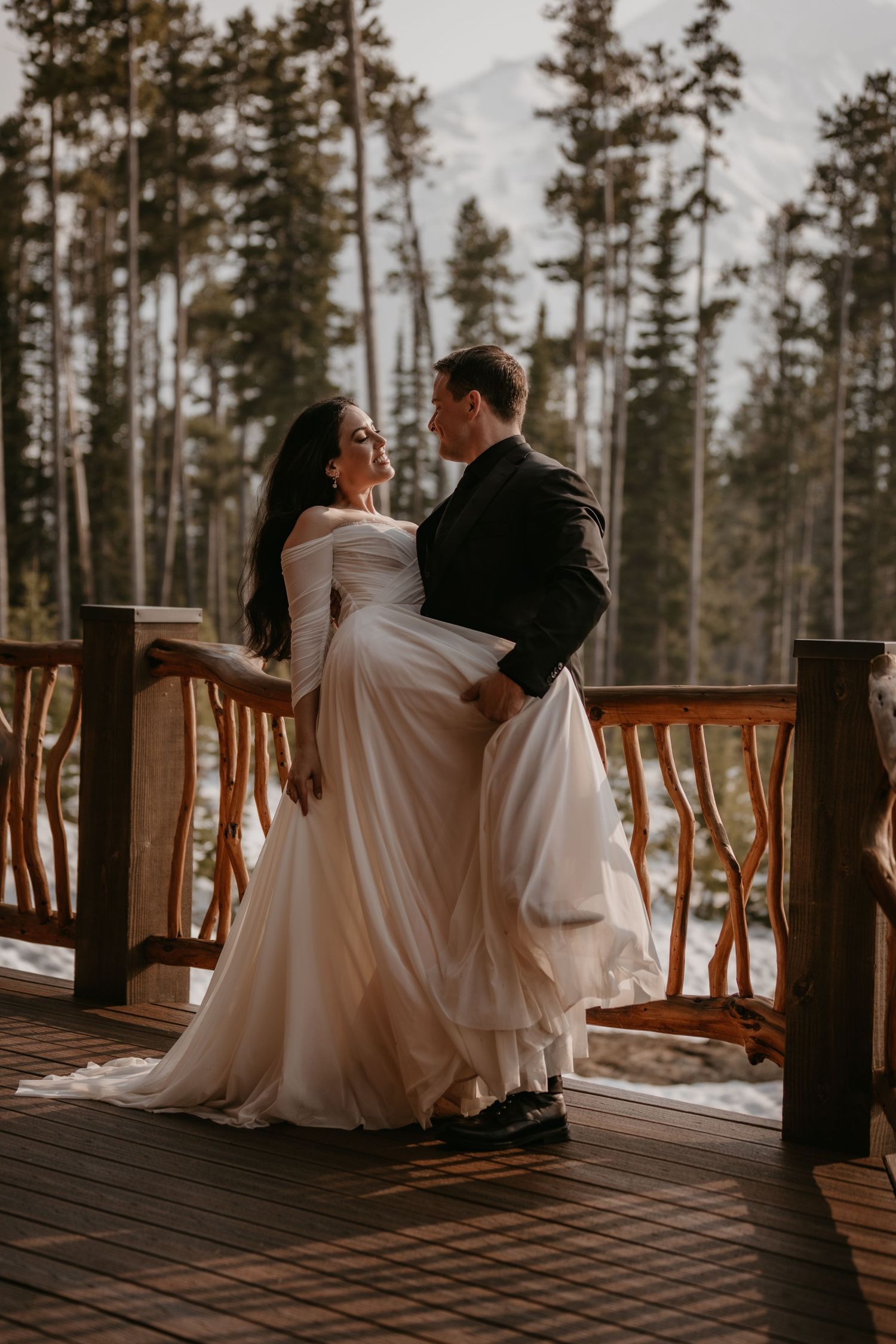 Wedding couple sharing tender moments on a wooden deck with mountain scenery.